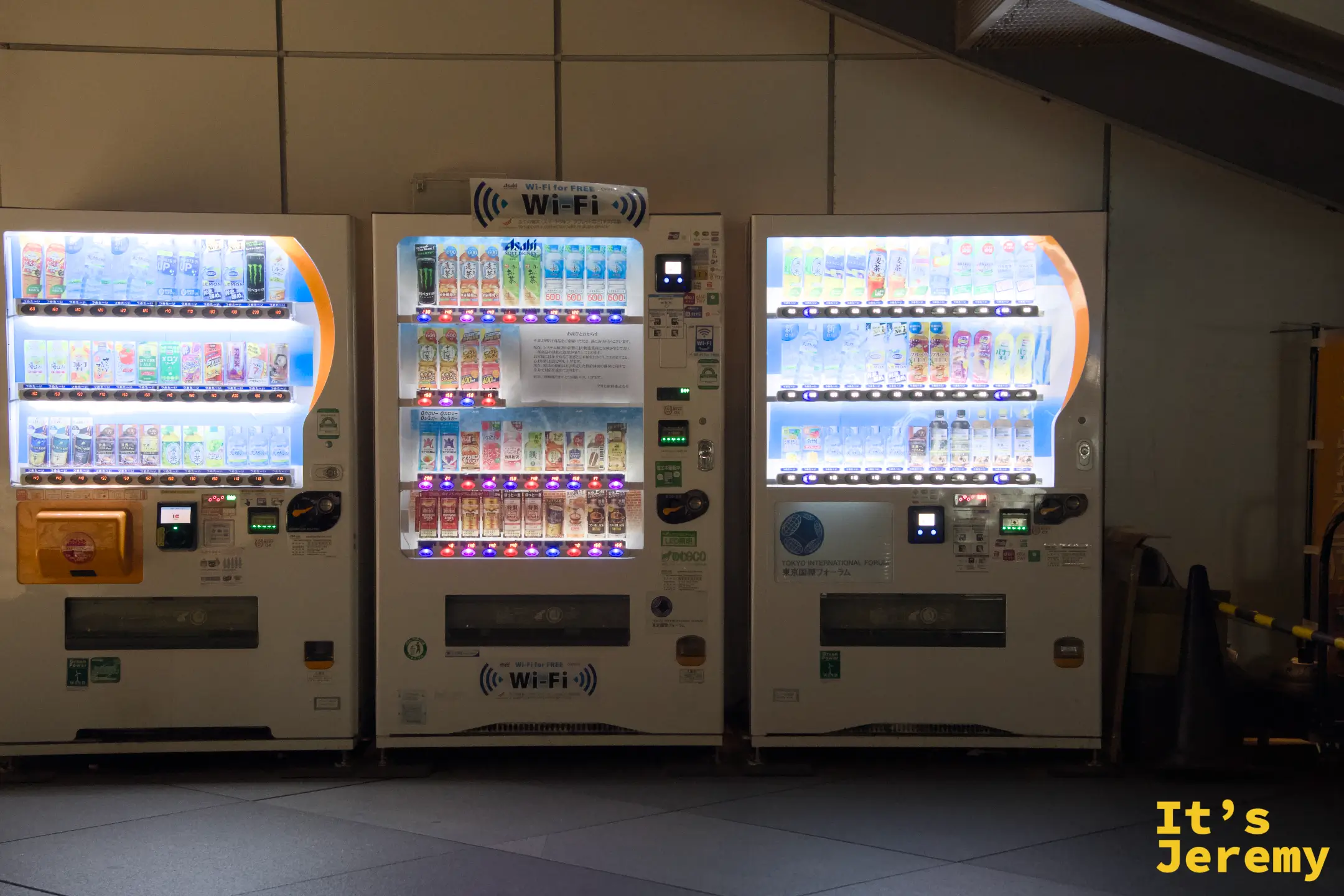東京國際論壇廣場內,三台白色自動販賣機並排,中間台設有 Wi-Fi 分享功能,Asahi 品牌飲料整齊排列
