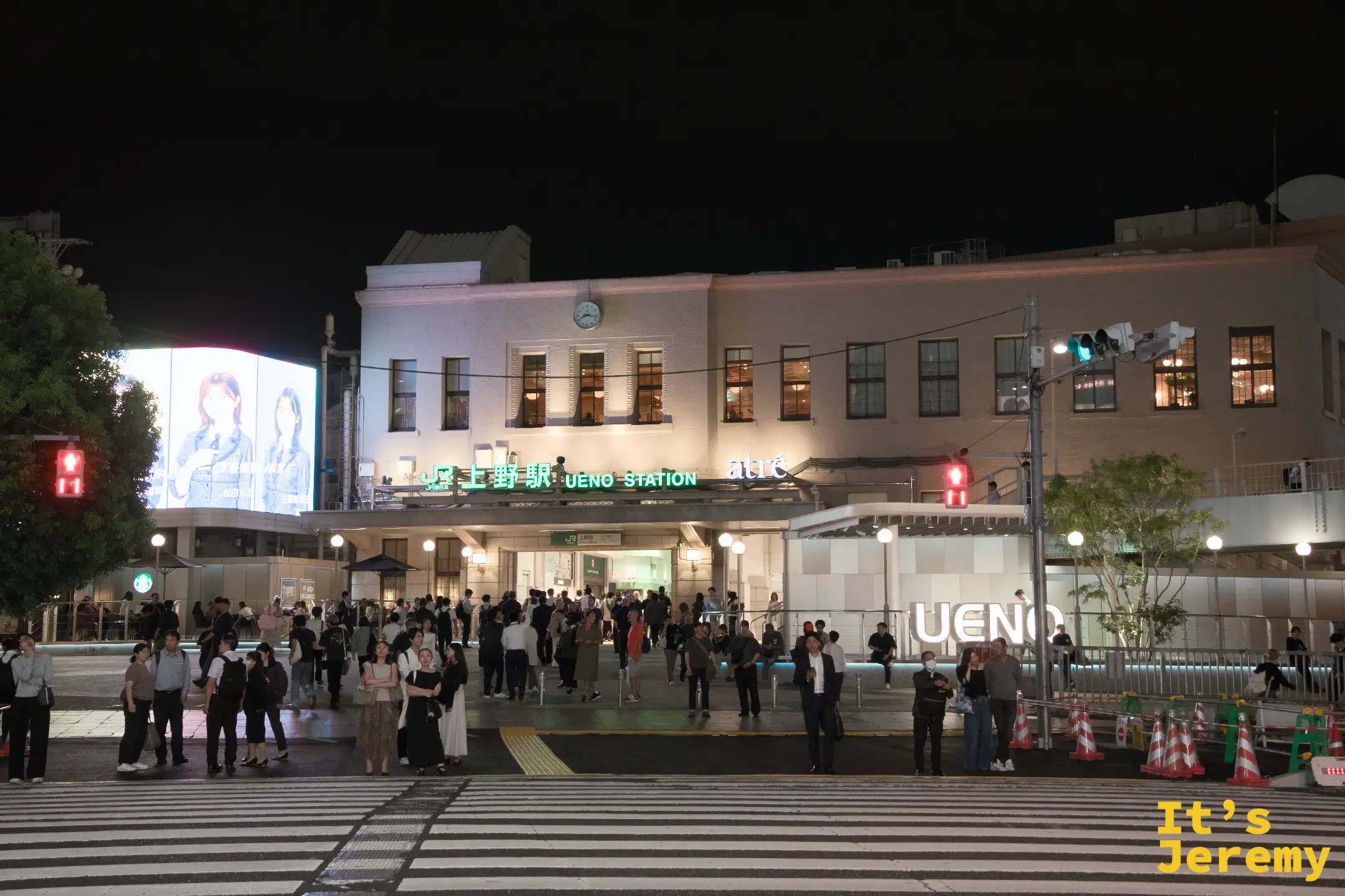 上野駅正面全景夜拍,車站白色建築打燈,UENO STATION 招牌明亮,廣場前人群聚集,廣告大螢幕在左側播放