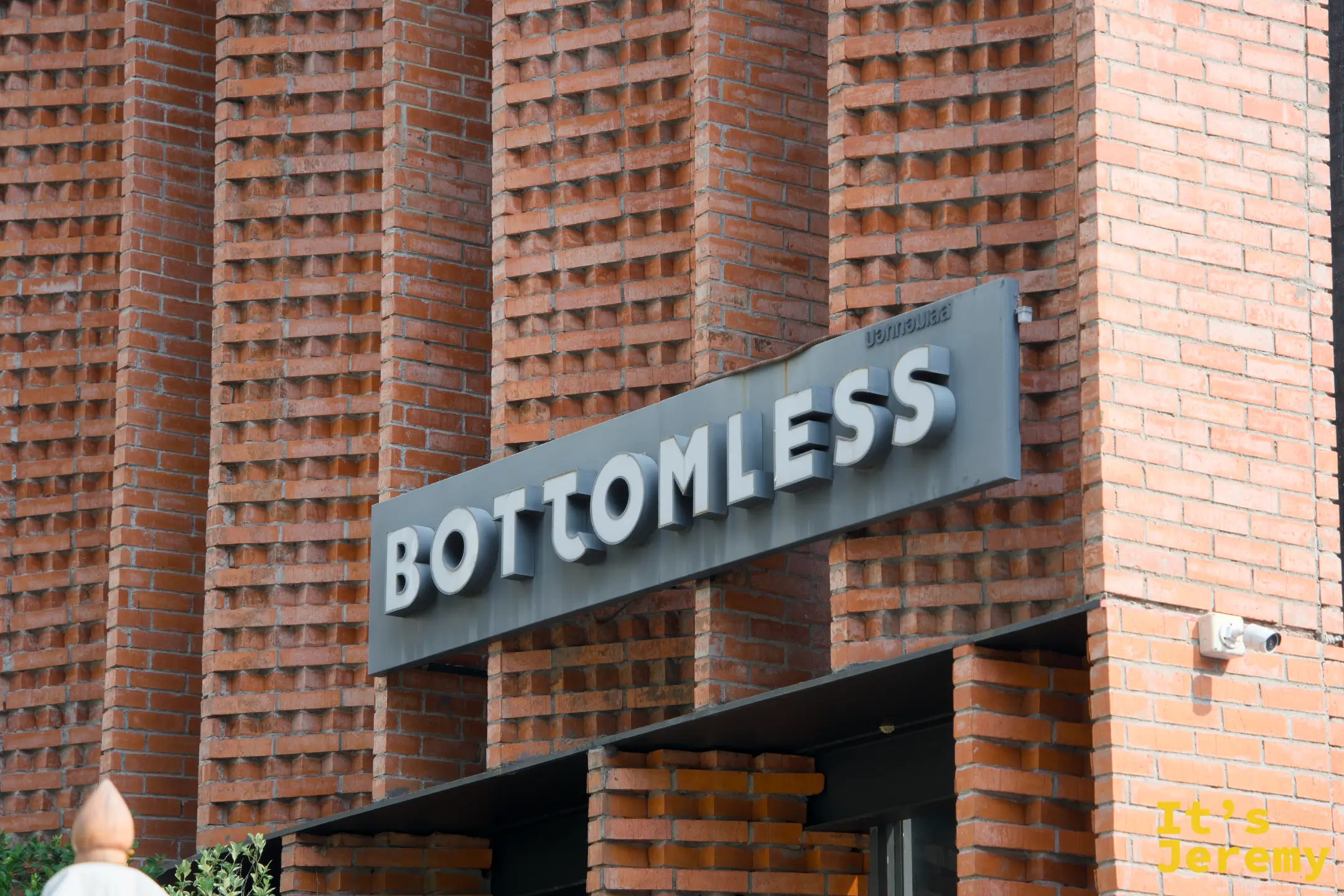 建築主入口旁的 BOTTOMLESS 金屬字招牌，鑲嵌在紅磚牆上