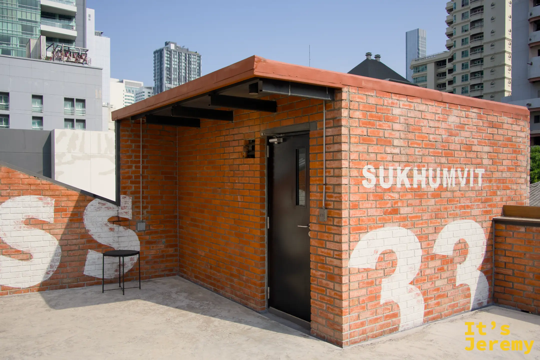 三樓天台出口磚房，上面寫有「SUKHUMVIT 33」字樣，旁邊有一把椅子