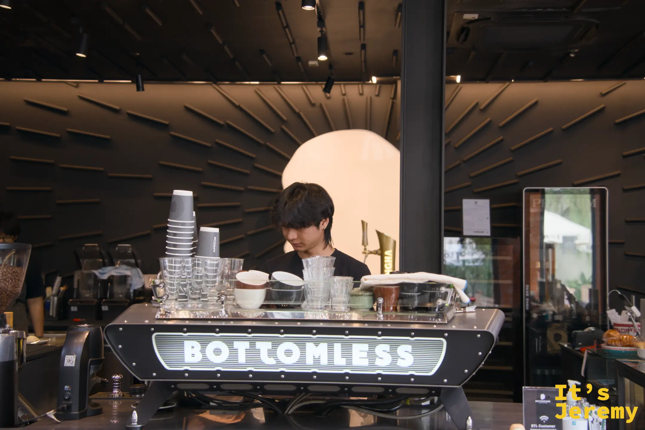 BOTTOMLESS 一樓主咖啡機，機身印有白色霓虹招牌字，背後有咖啡師在工作