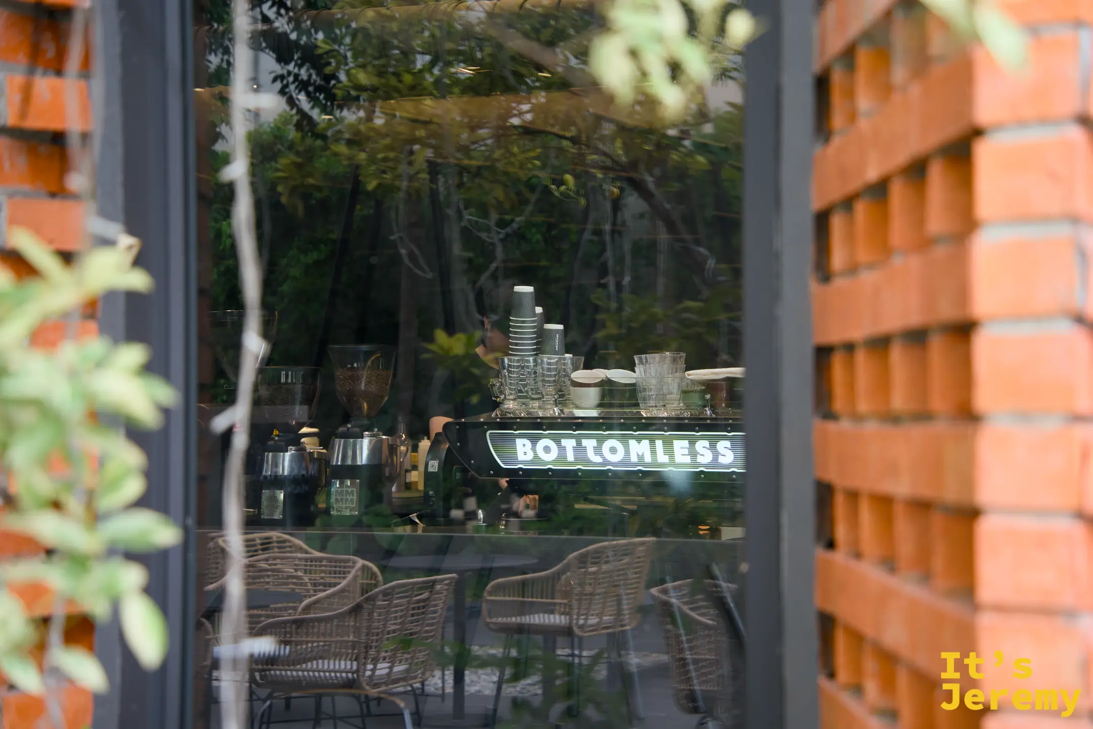 從戶外透過玻璃窗看見 BOTTOMLESS 咖啡機，樹枝倒影疊在玻璃上