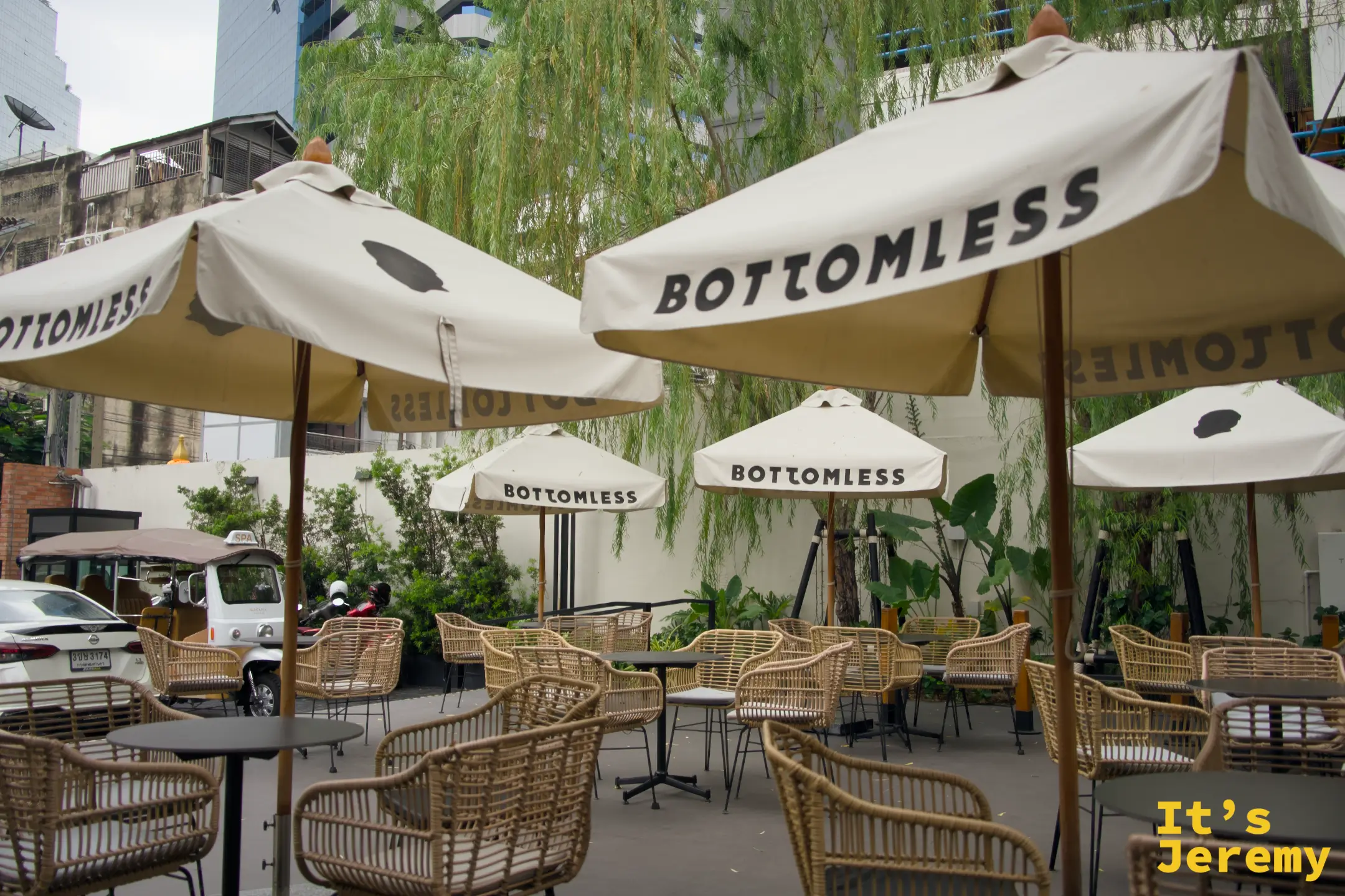 戶外庭院另一角度，多把 BOTTOMLESS 品牌傘排列，背後可見曼谷街景
