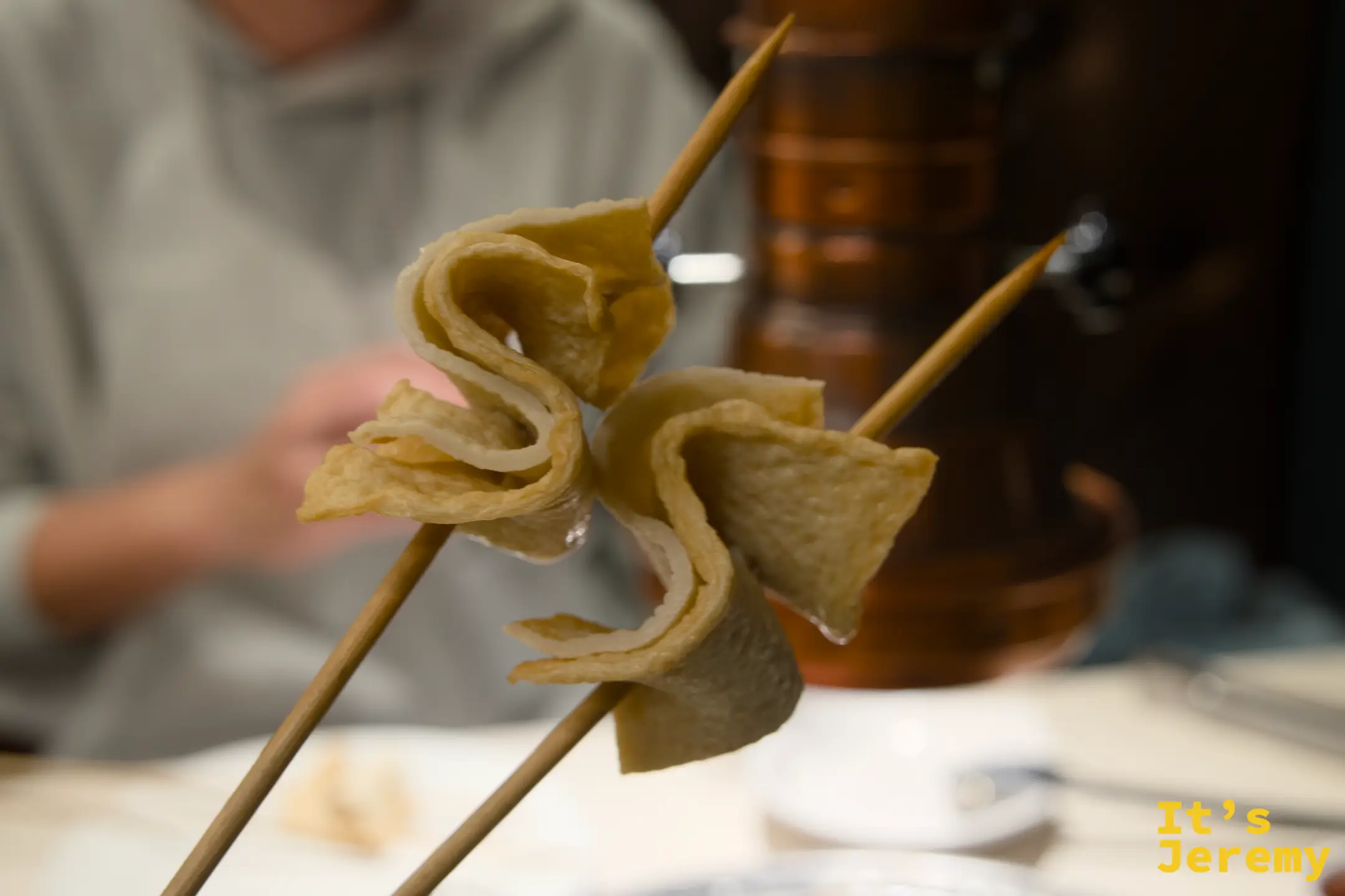 竹籤串著剛烤好的돼지껍데기，外皮微鼓酥脆，用筷子夾起展示的樣子