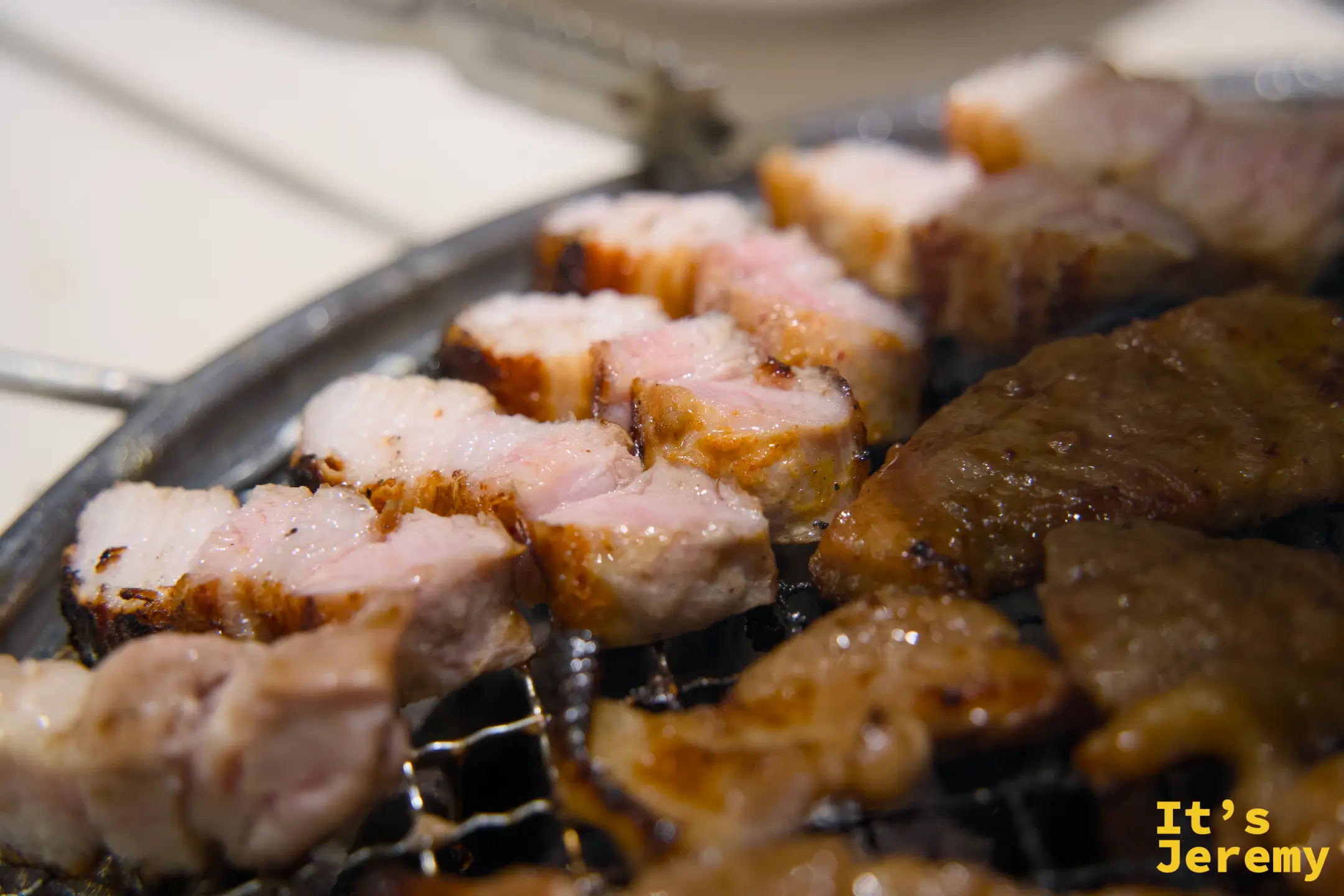 烤爐上的삼겹살與갈비肉塊，油脂滋滋冒泡，邊緣呈現漂亮的焦糖色