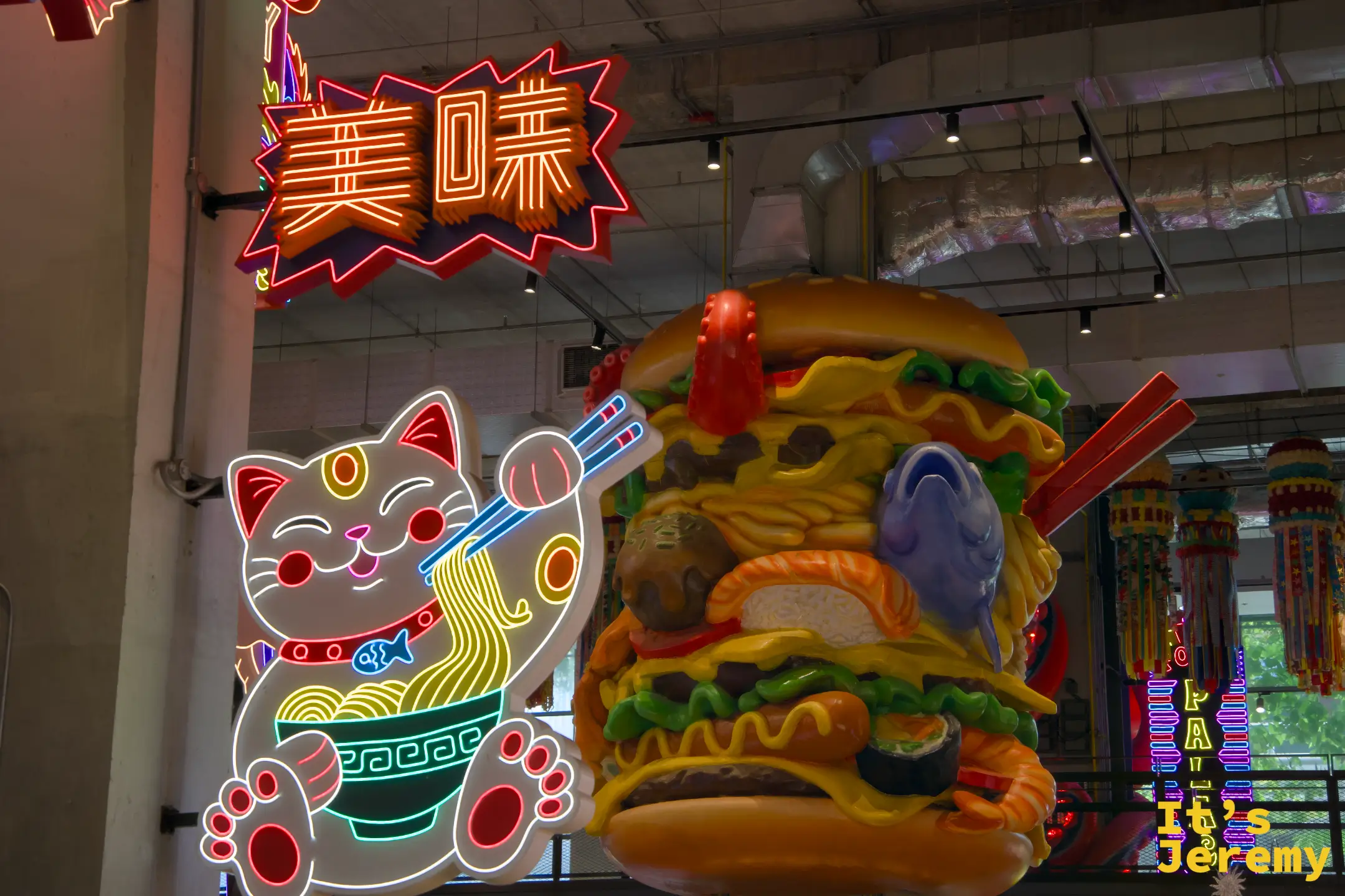招財貓吃拉麵的霓虹燈牌與「美味」霓虹字樣,右邊是巨型食物混搭雕塑