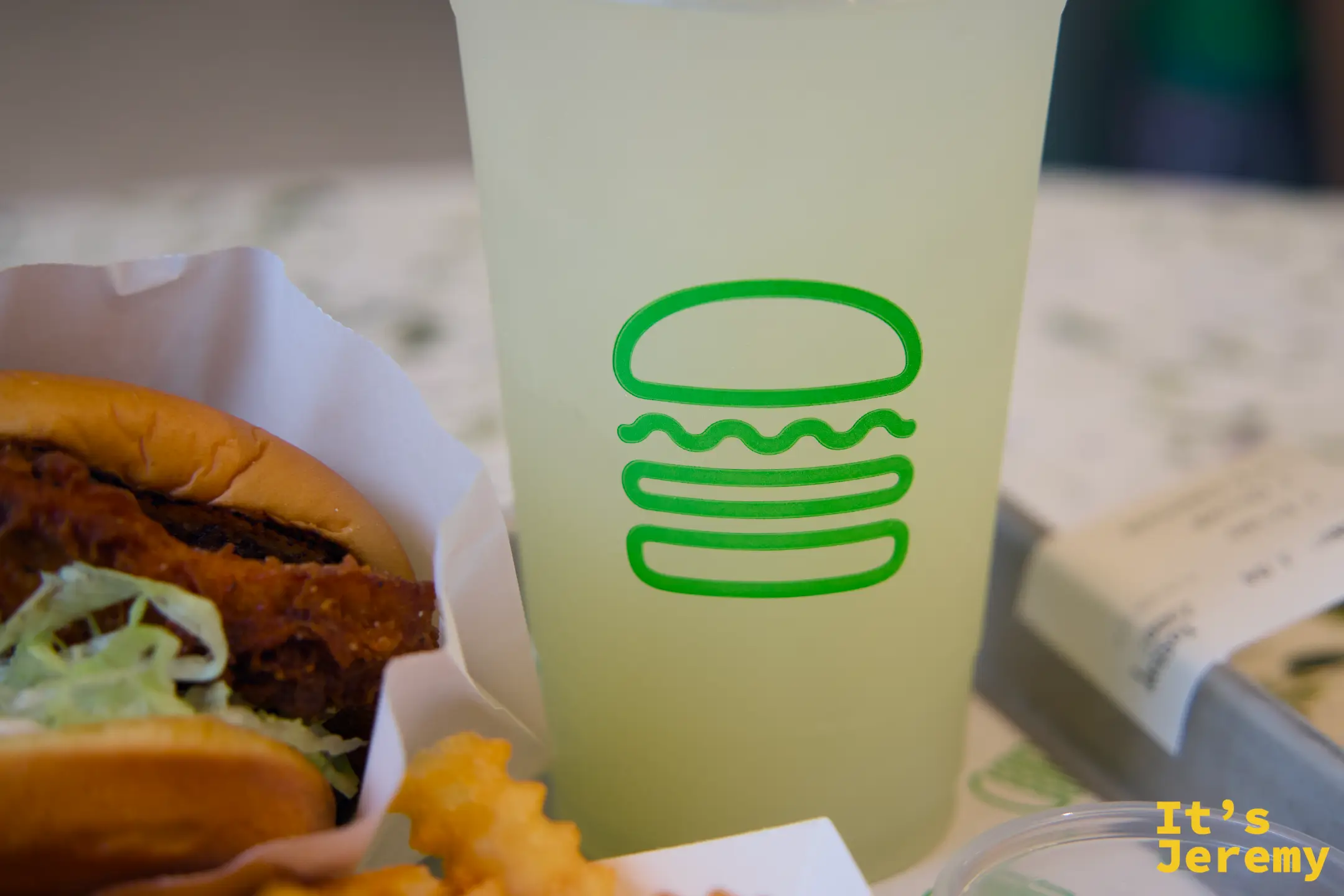 Shake Shack 大杯 Lemonade 特寫，淡黃色清澈飲料裝在印有綠色漢堡 logo 的杯子裡