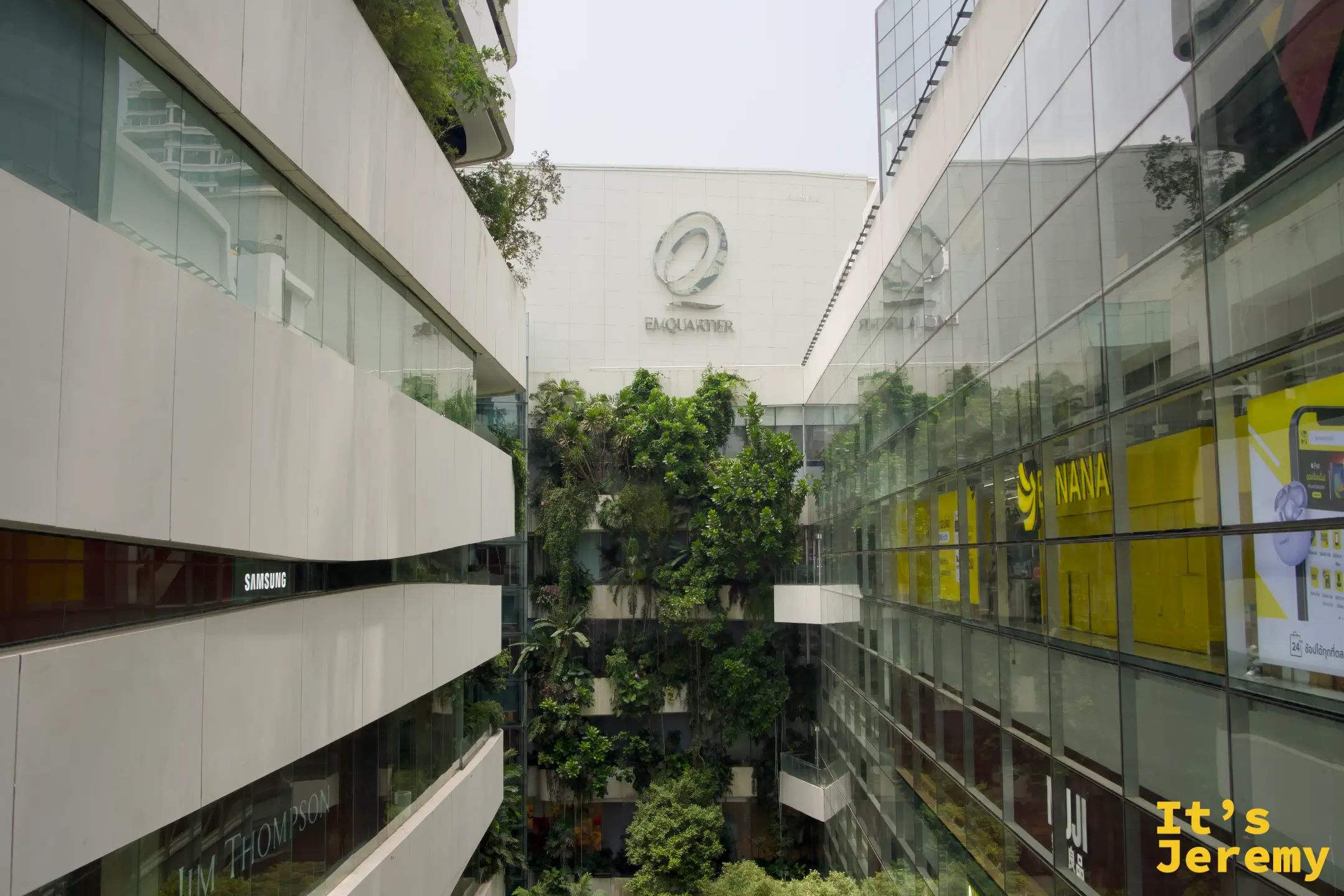 EmQuartier 中庭俯視,兩棟玻璃建築夾著綠意中庭,可見 EmQuartier logo、Jim Thompson 等品牌招牌