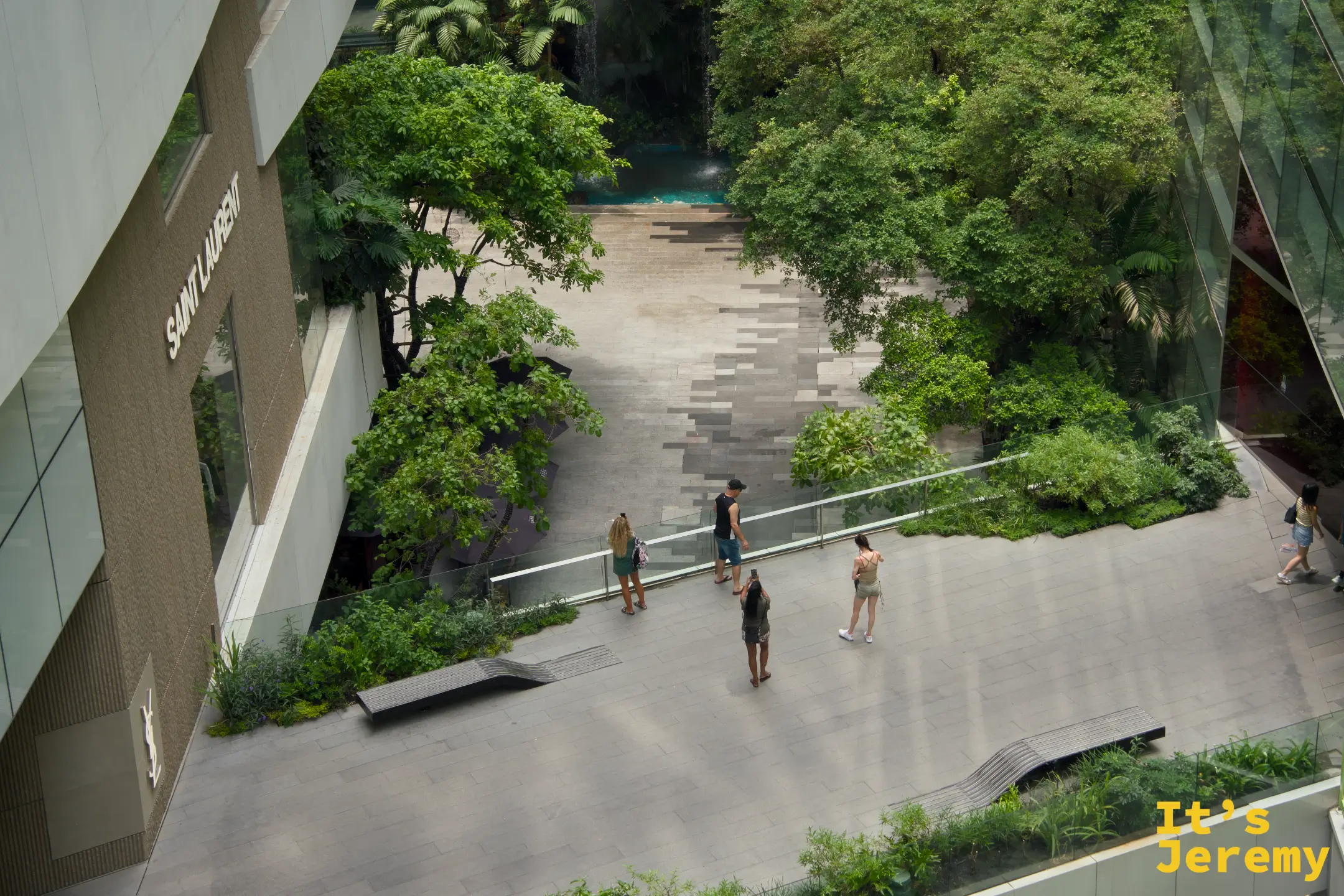 EmQuartier 戶外花園廣場,石板地面,有旅客在樹下走動或站立