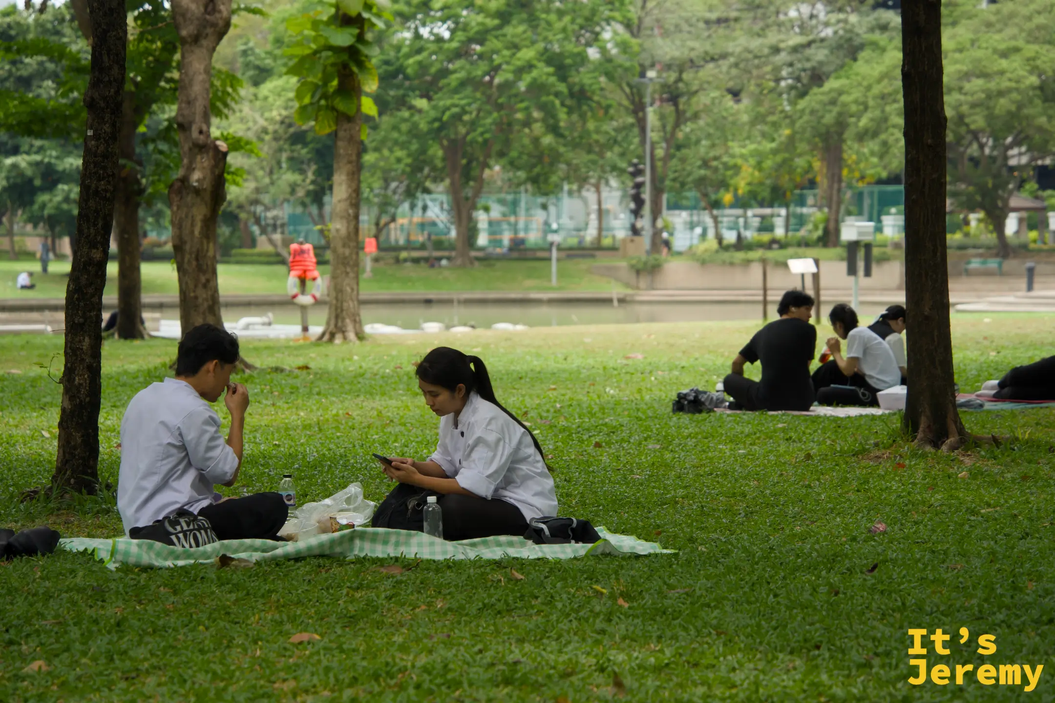 兩名穿制服的學生坐在班哲希利公園草地上,其中一人滑手機