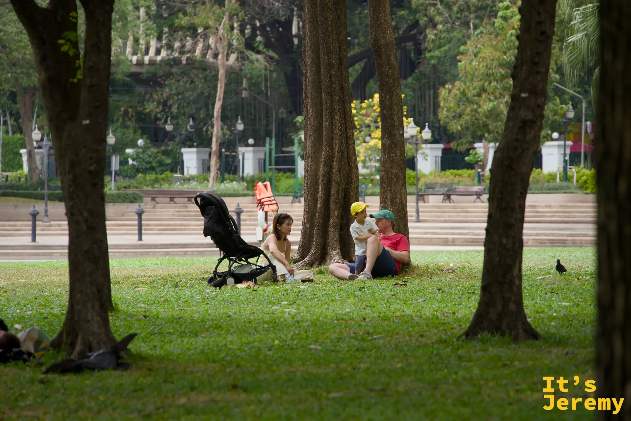 班哲希利公園,一對夫妻帶嬰兒車在大樹下草地旁休息,小孩坐在樹旁