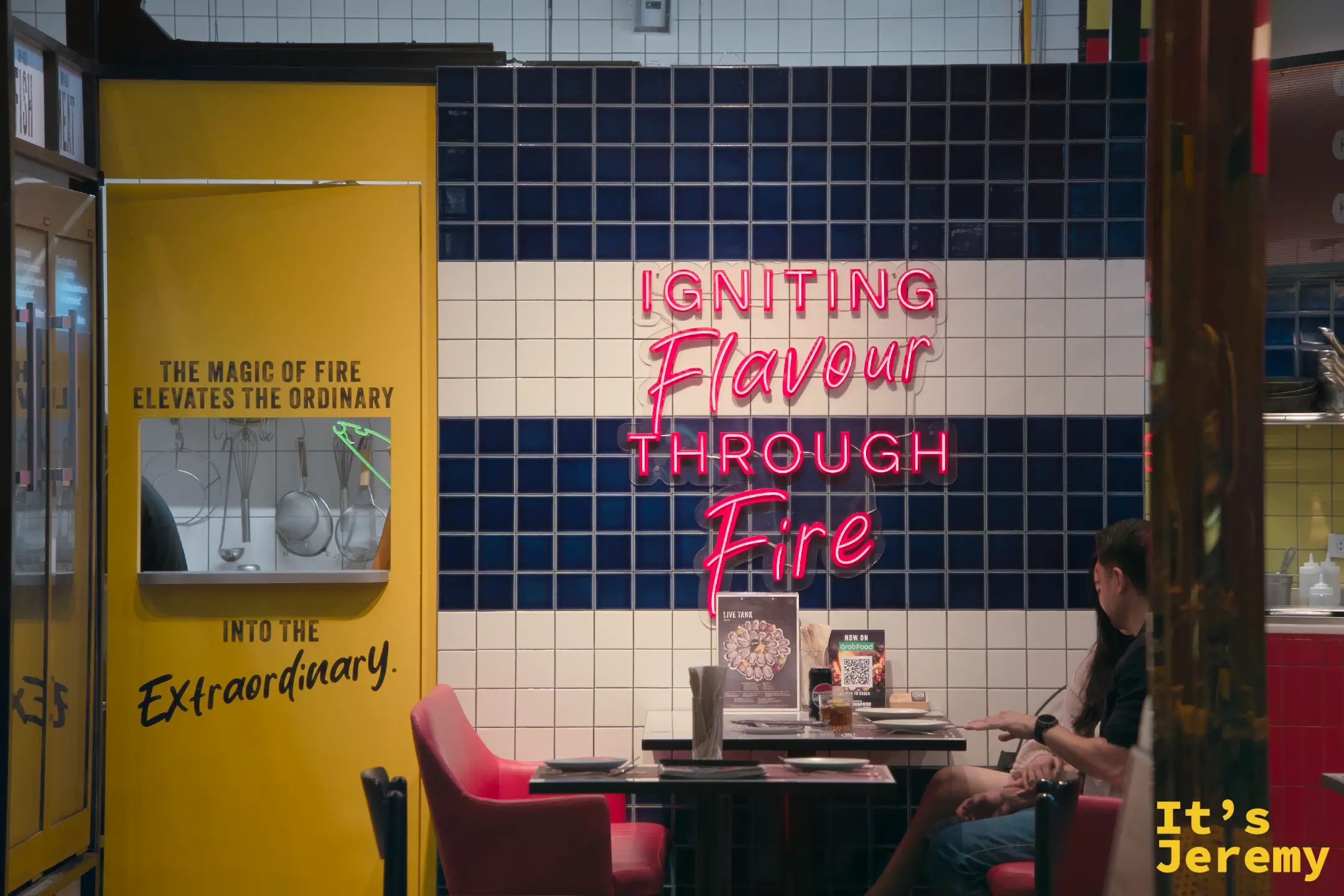 餐廳入口,藍白磁磚牆上霓虹「Igniting Flavour Through Fire」字樣,橙色椅子,食客就座