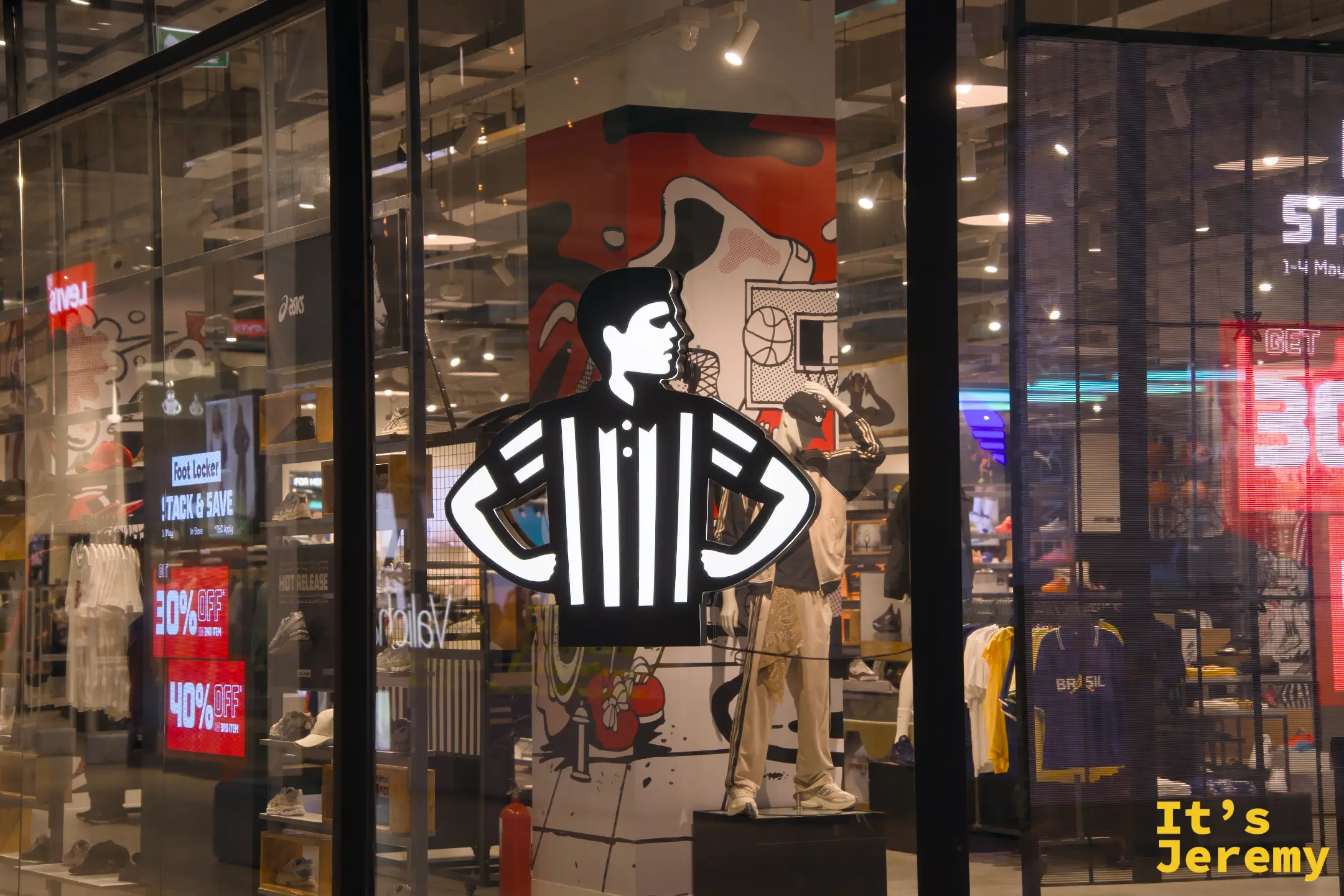 Foot Locker 夜晚櫥窗,霓虹裁判員剪影,背景可見多個運動品牌的鞋款陳設
