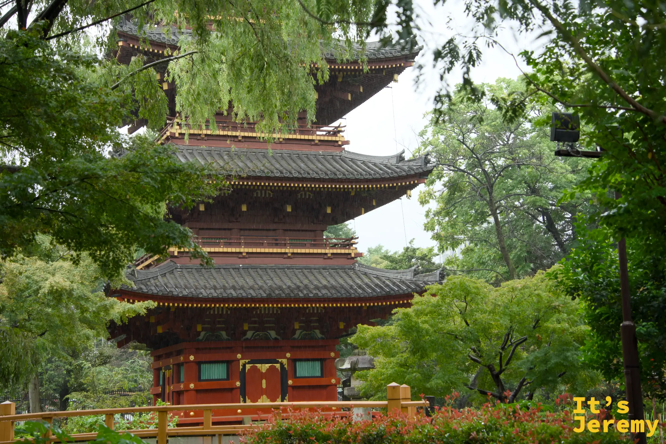 五重塔正面遠景,紅色塔身在翠綠樹木中很有分量,塔前有小橋和花叢