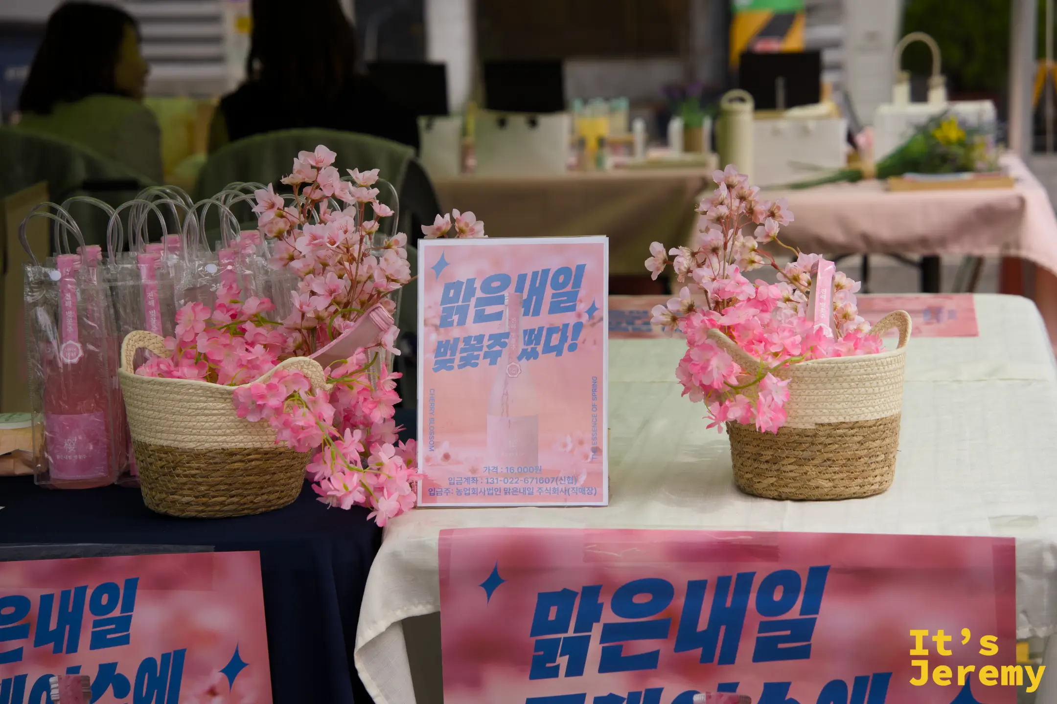 軍港祭的紀念品攤以粉色為主調,販售仿真粉花裝飾和花季特色包裝飲品,連牌子上的字都透著春天的氣息