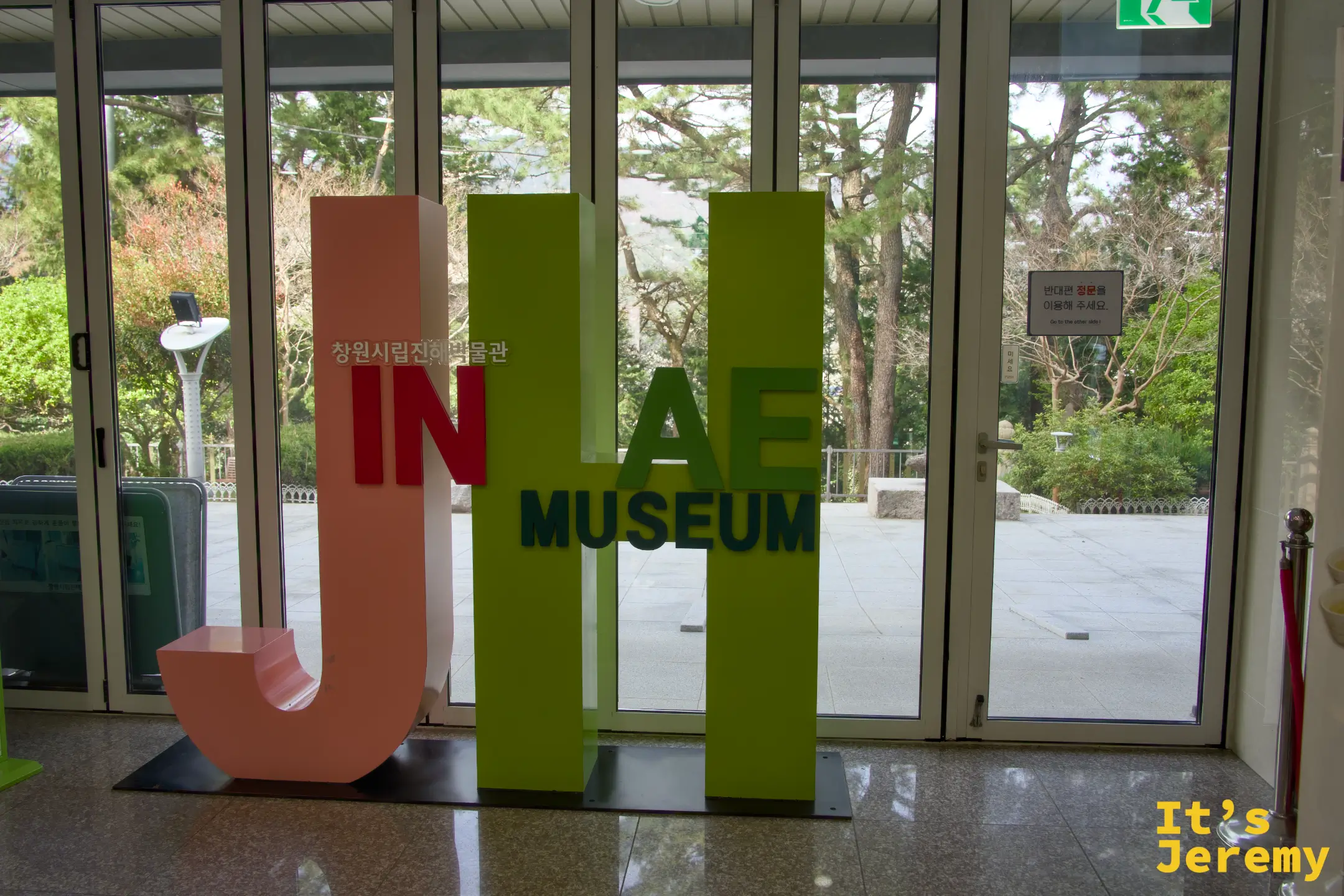 昌原市立鎮海博物館館內大廳,JINHAE MUSEUM 字樣裝置立於入口,落地窗外透著春日的綠意