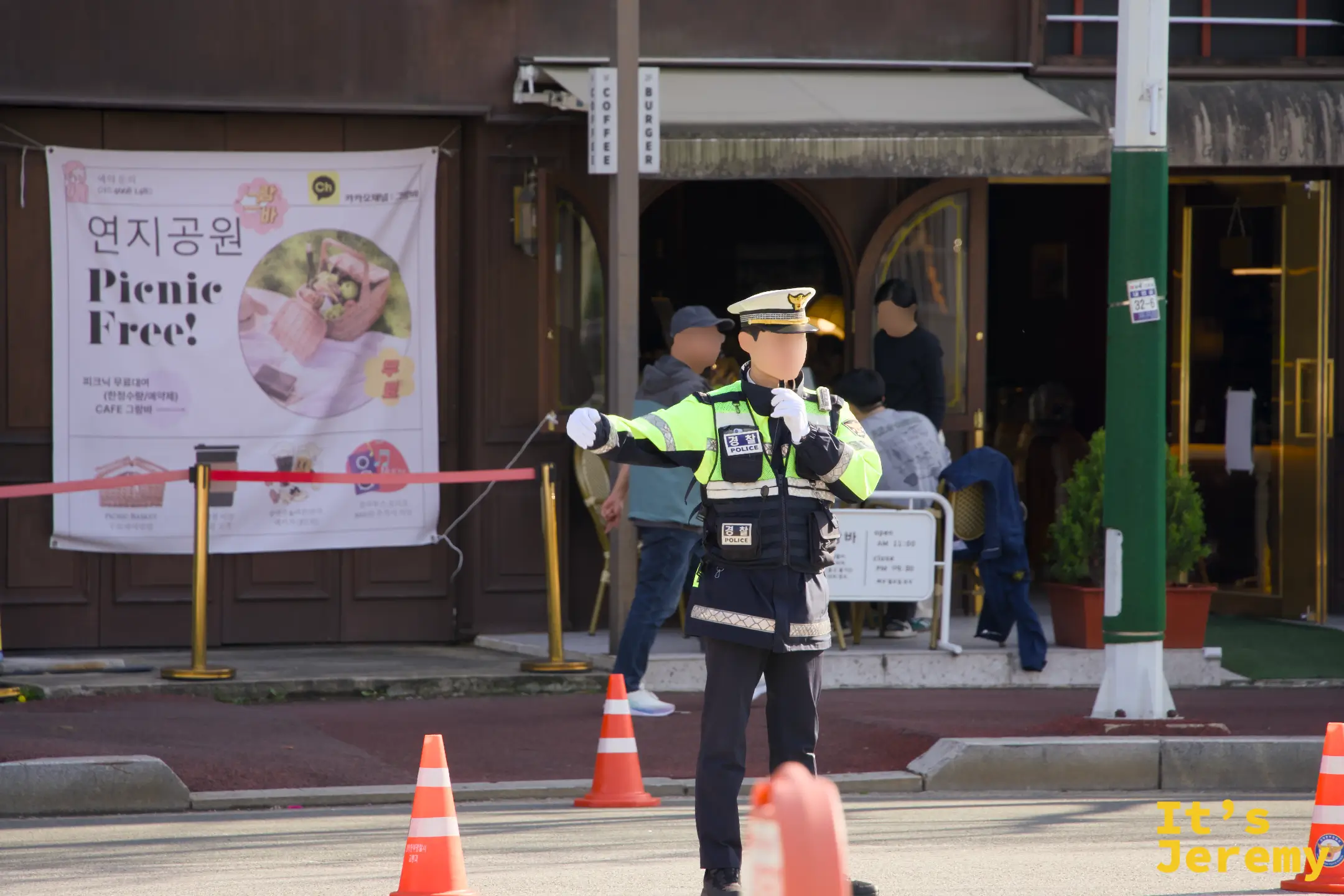 春祭當天公園入口附近，交警指揮交通，後方咖啡館外牆掛著「연지공원 Picnic Free！」活動海報