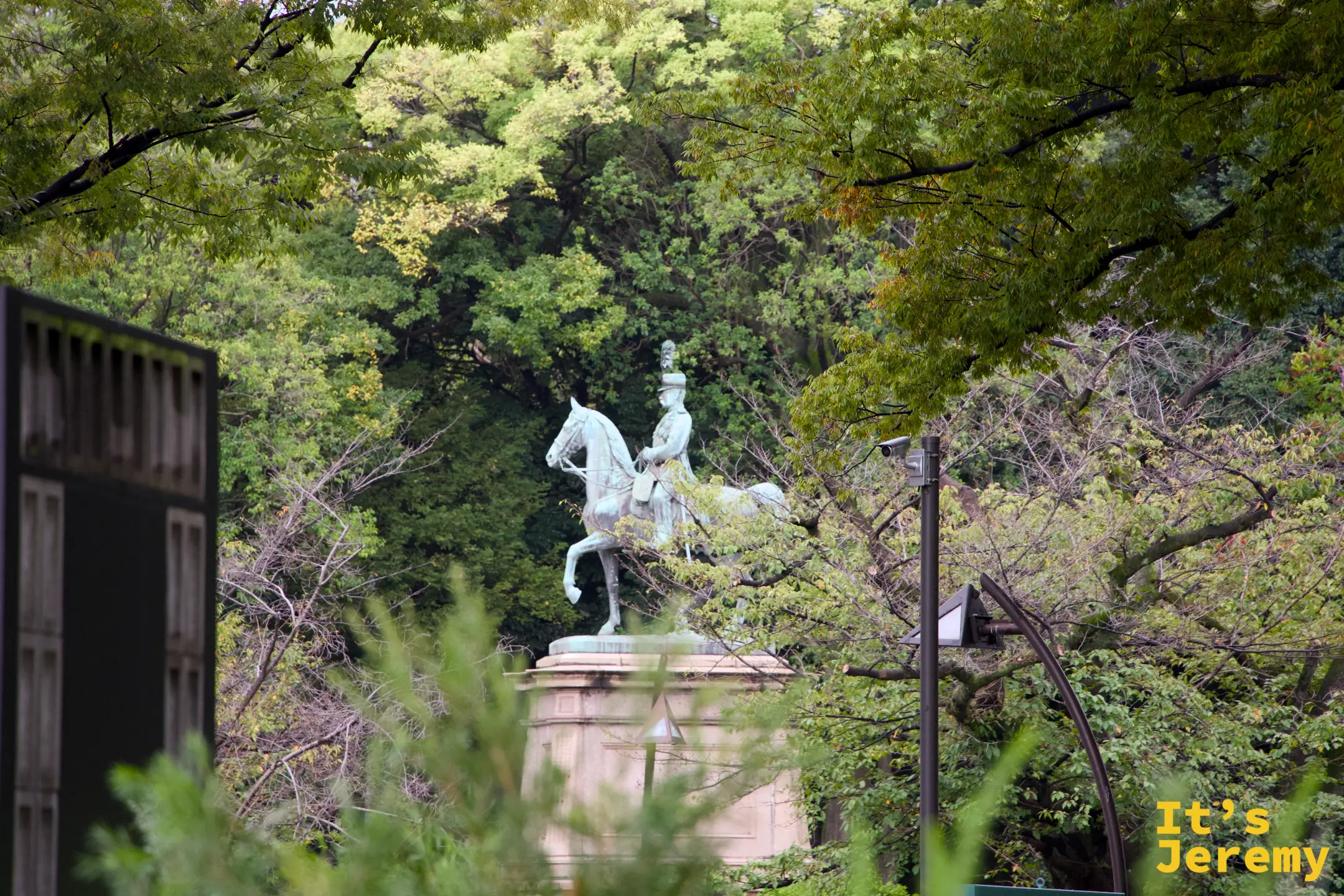 上野公園附近的騎馬銅像,青銅色的人馬雕塑在翠綠樹木的環繞之中,背景天空帶著淡淡的霧氣