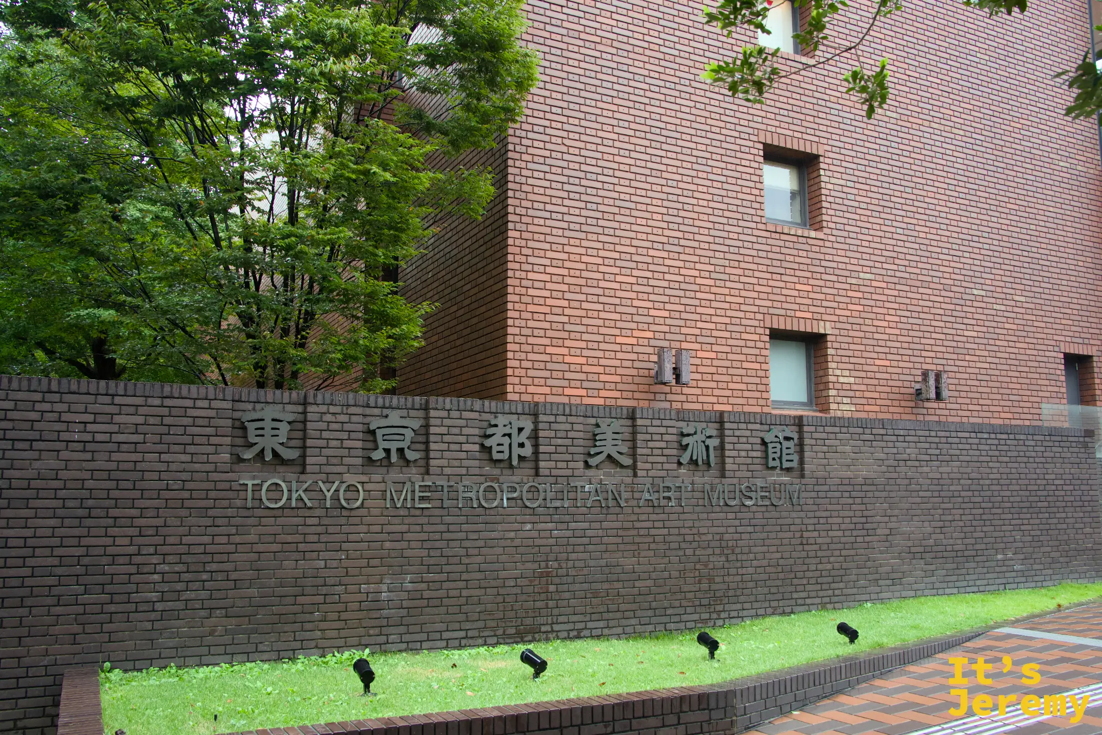 東京都美術館外牆的「東京都美術館 TOKYO METROPOLITAN ART MUSEUM」字樣牌匾,磚紅色外牆配上深綠色植栽