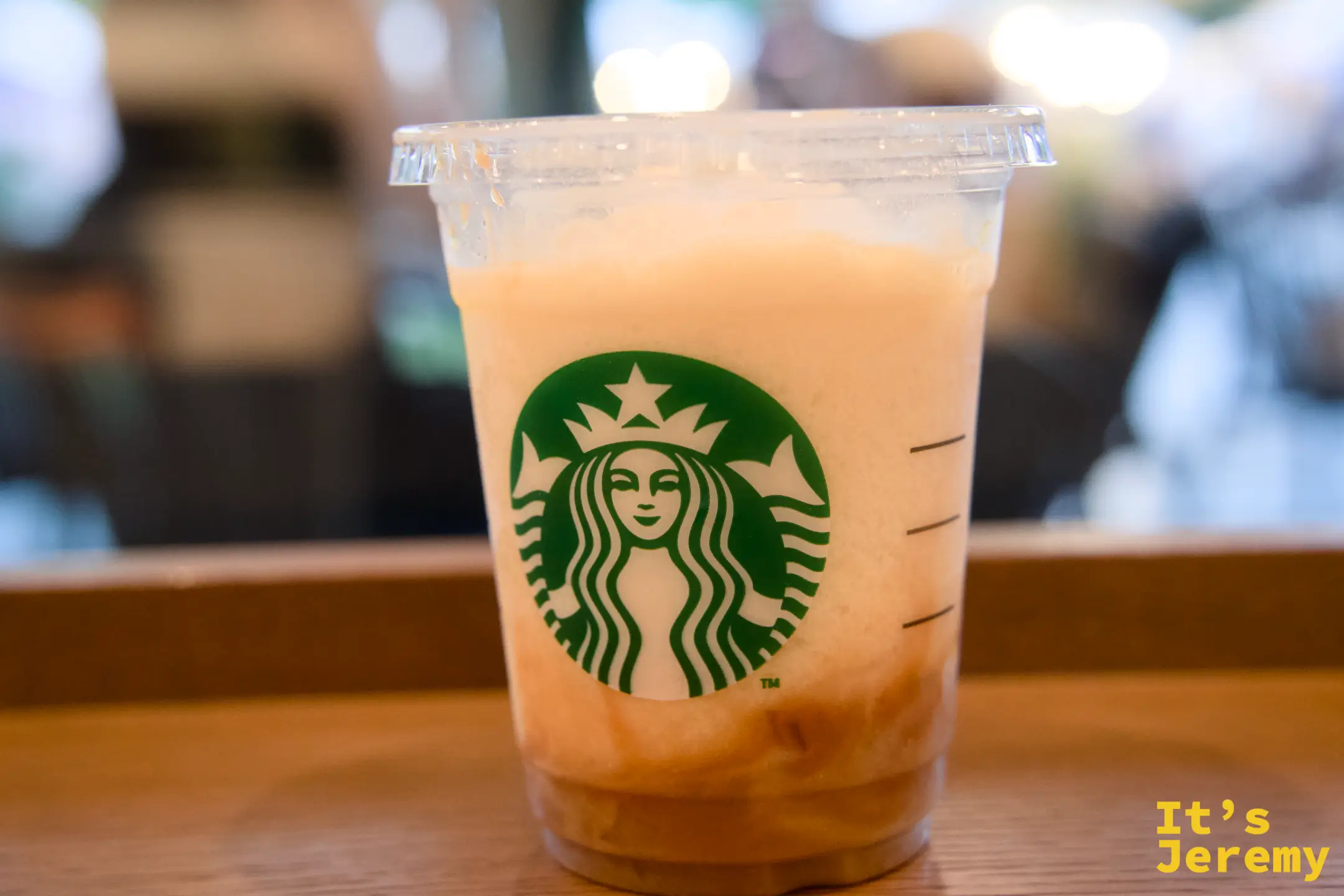 星巴克洋なし生キャラメルフラペチーノ,橘黃色奶泡的飲料放在木桌上,星巴克綠色女神 logo 清晰可見