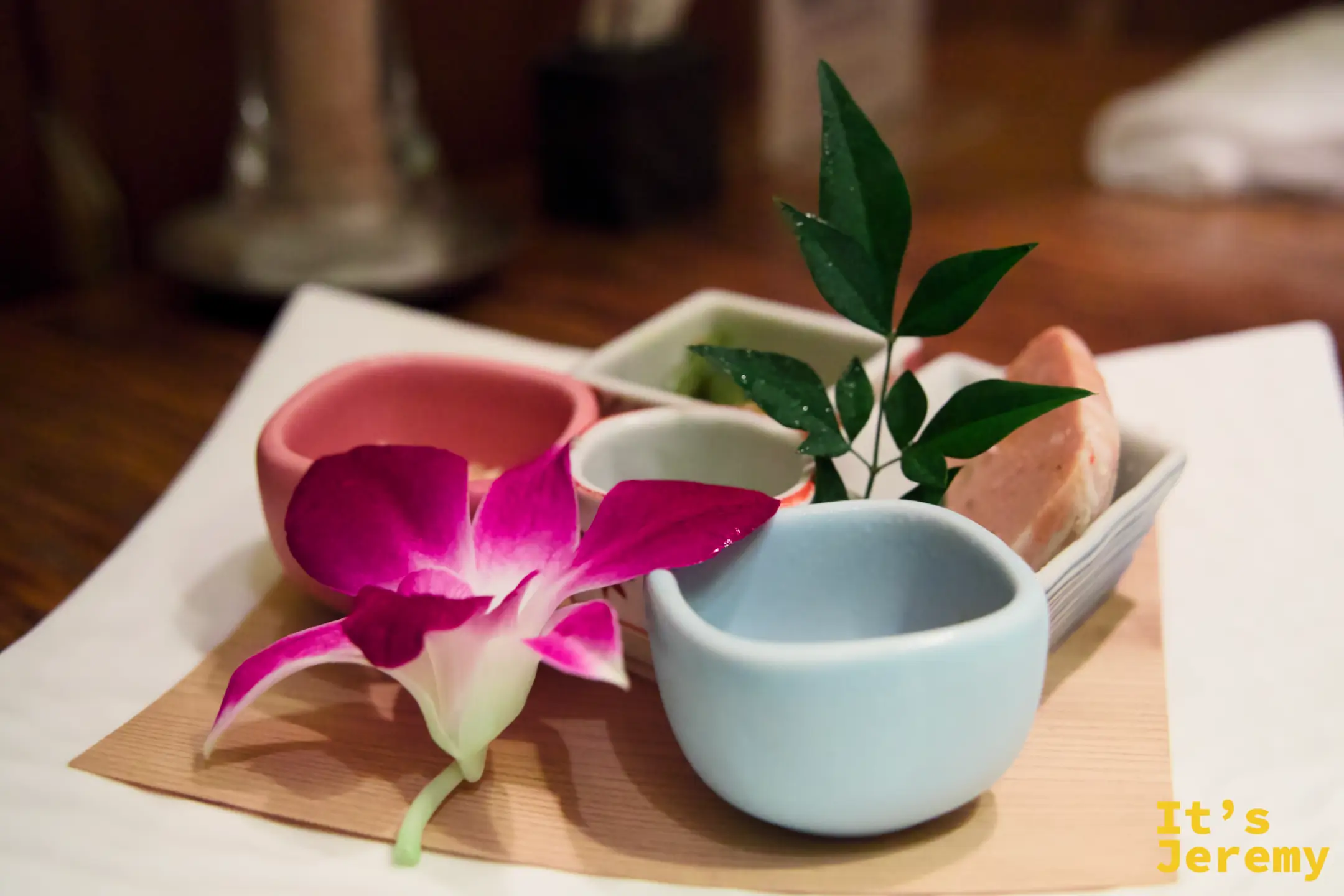 入座後送上的先付前菜，多個小陶碗排列在木托盤上，粉紅蘭花裝飾