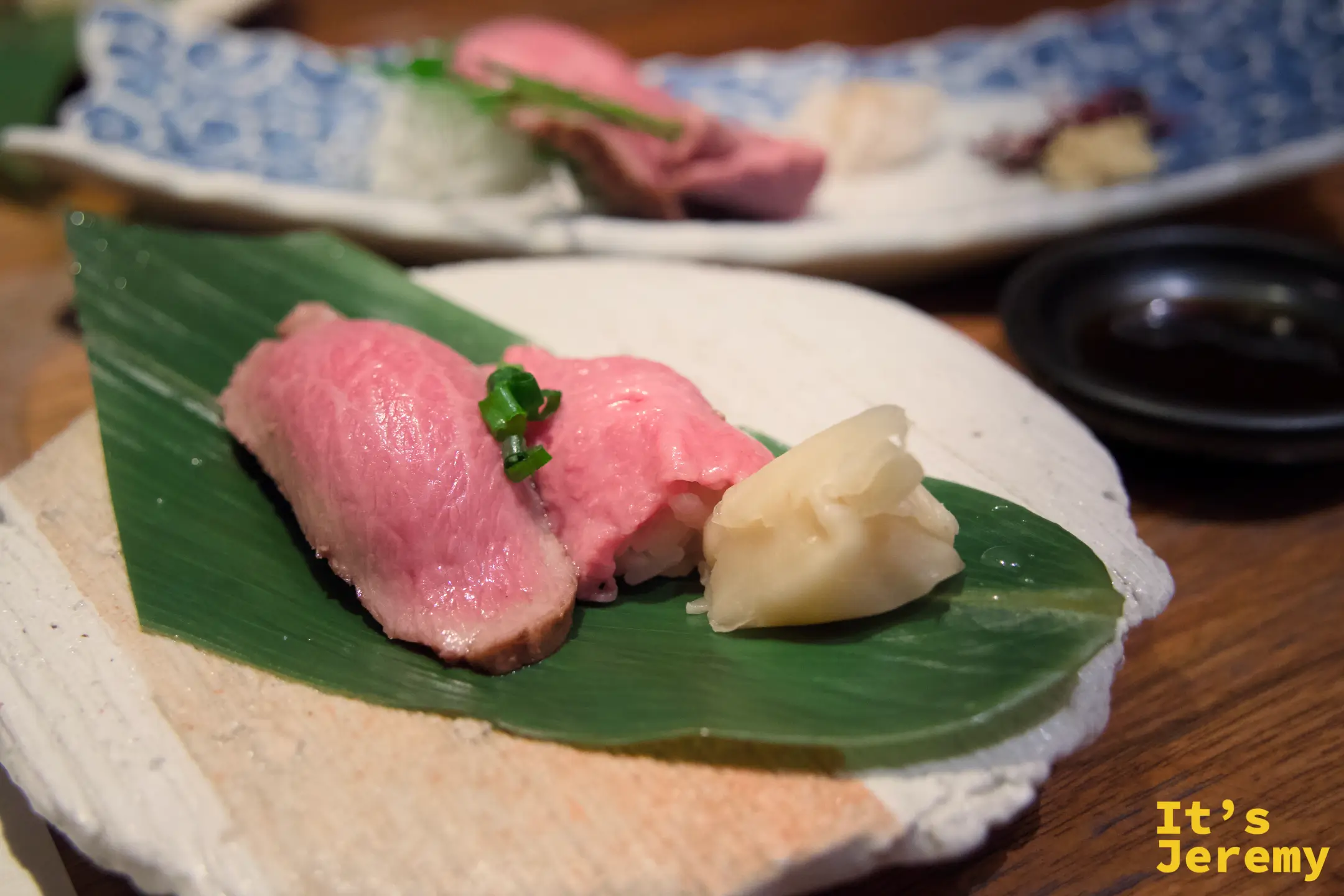 飛騨牛握壽司，霜降肉片置於竹葉盤上，旁附薑片
