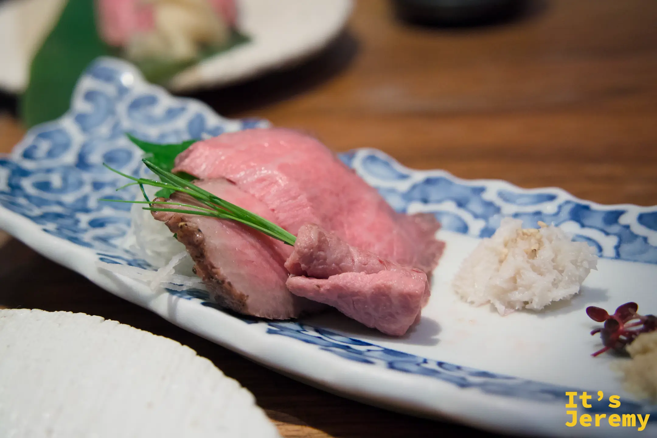 飛騨牛握壽司，藍白花紋陶盤，霜降肉片旁附白蘿蔔泥與芽苗菜