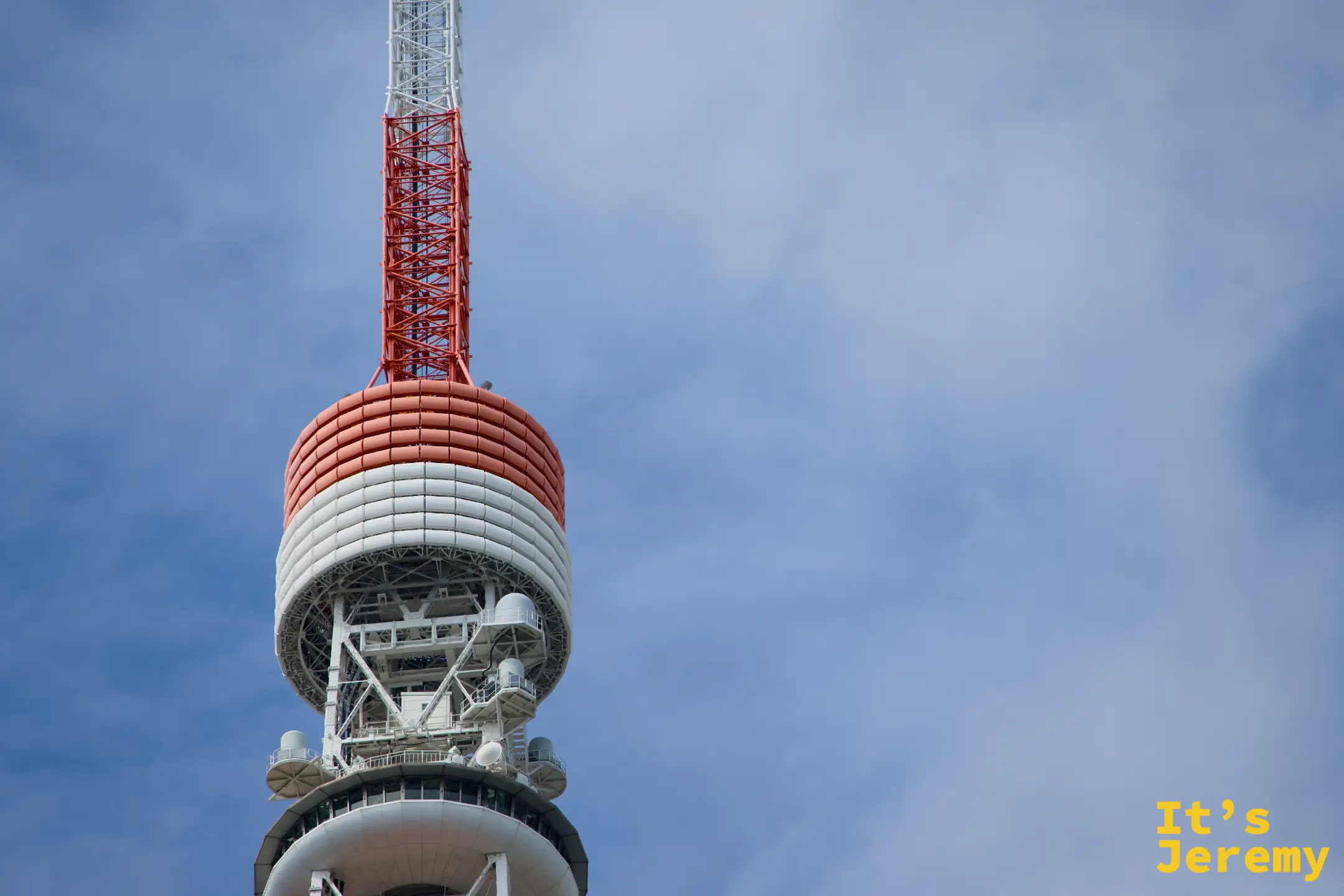仰望東京鐵塔頂端,特別展望台的渾圓弧形構造在鐵塔最高段隱約可見,其上的廣播天線繼續向天空伸展,整體拍攝帶有明顯的仰角壓縮感