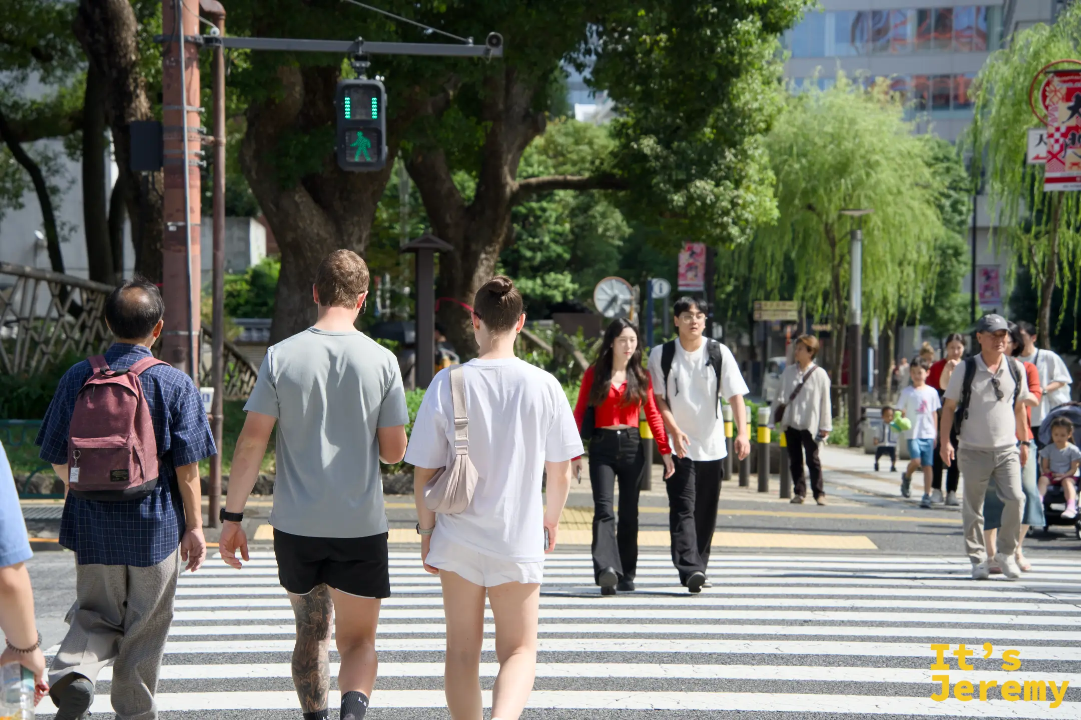 芝公園路口,人們走在開闊的人行道上,四周綠樹成蔭,東京的上午