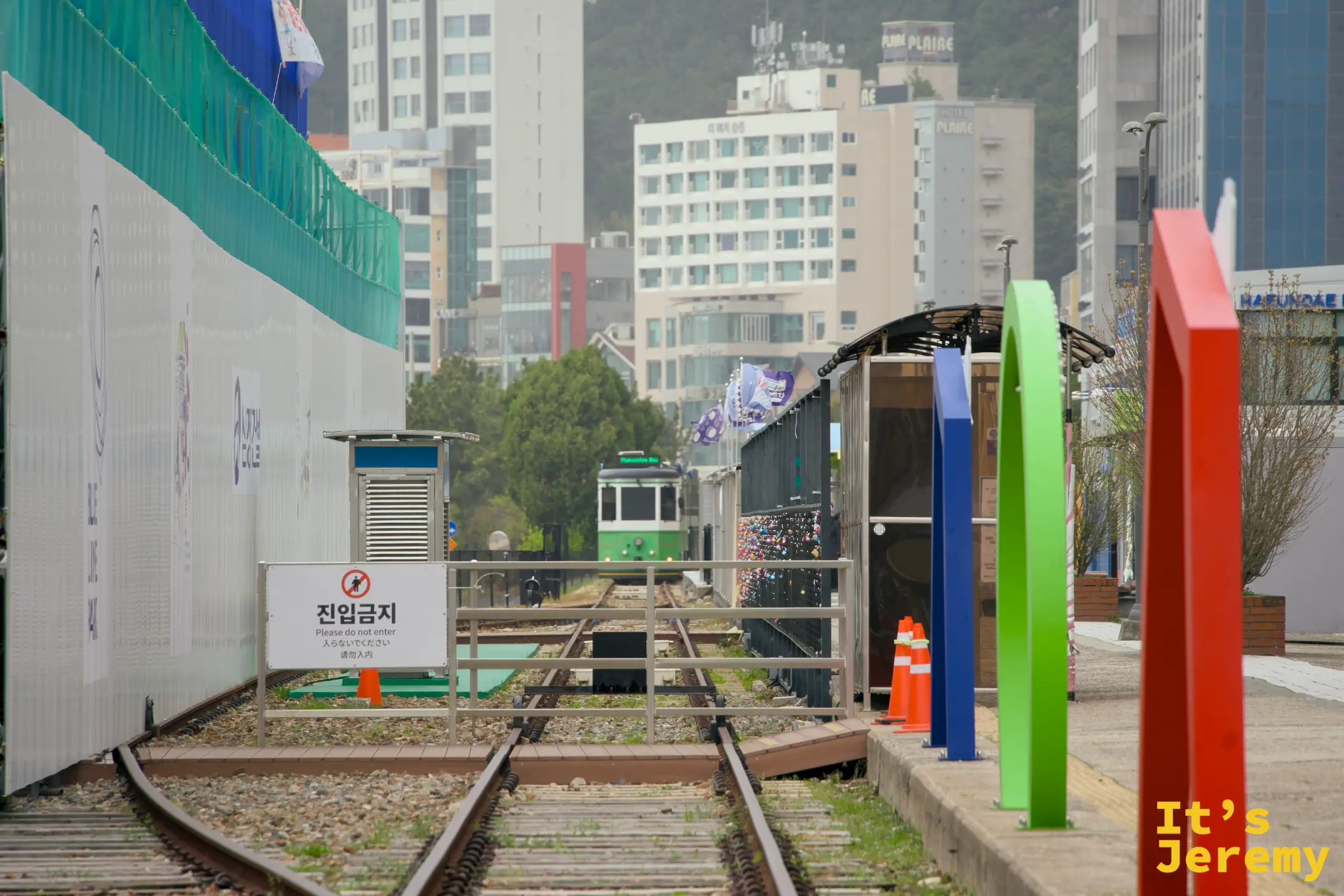綠色海岸列車沿著雙軌鐵路緩緩駛入松亭站，右側可見掛滿愛情鎖的牆面