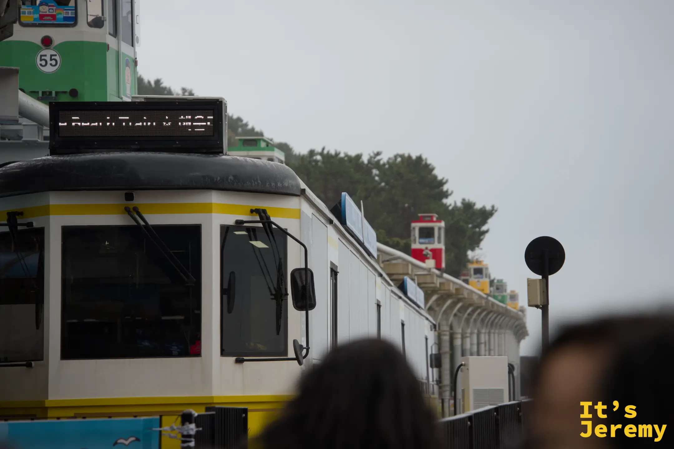 「Beach Train 해변열차」LED 字幕牌亮起，黃色與綠色海岸列車車廂並排等候出發
