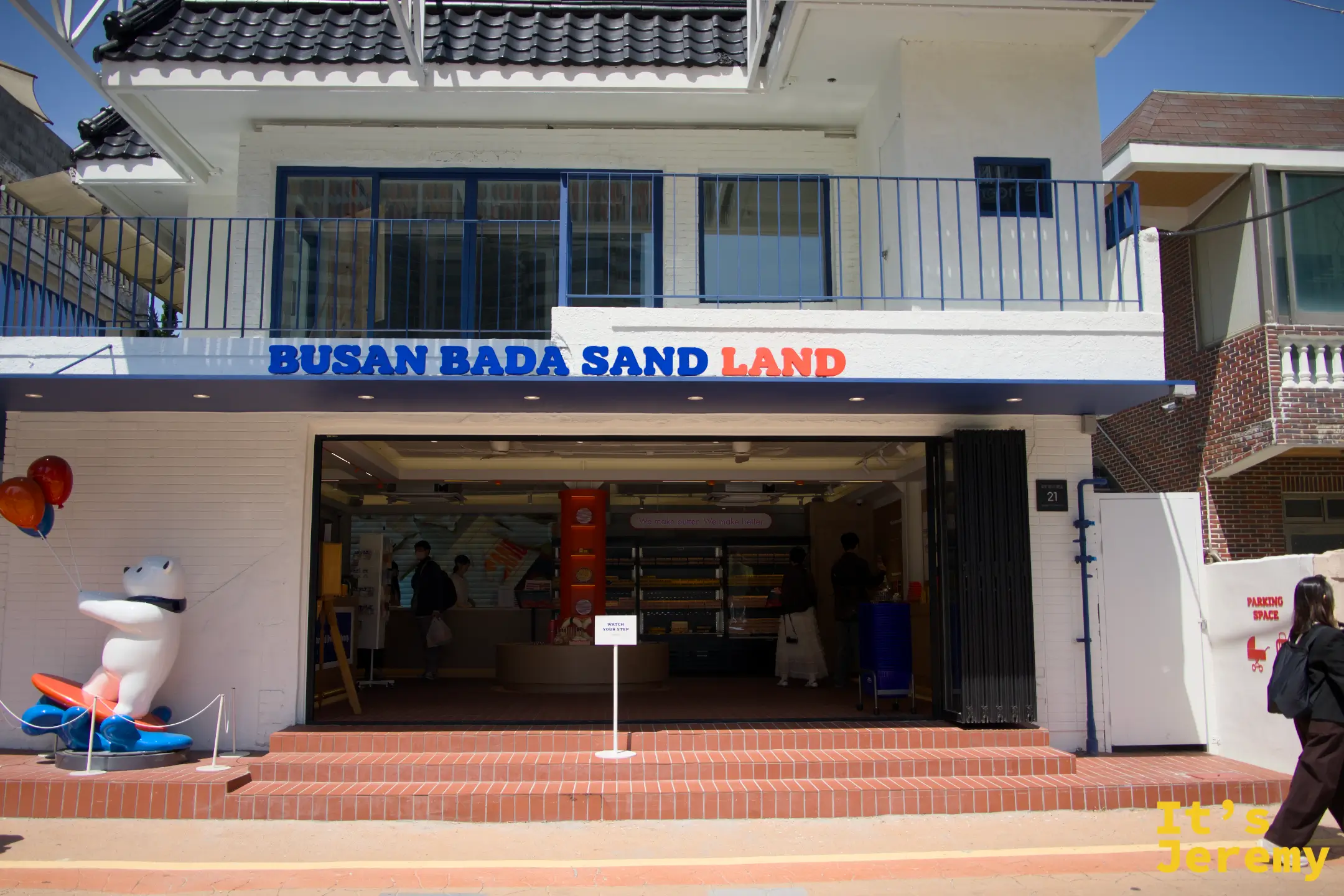 Busan Bada Sand LAND 藍白兩層樓外觀全景，入口左側是衝浪板造型的 Booba 北極熊吉祥物