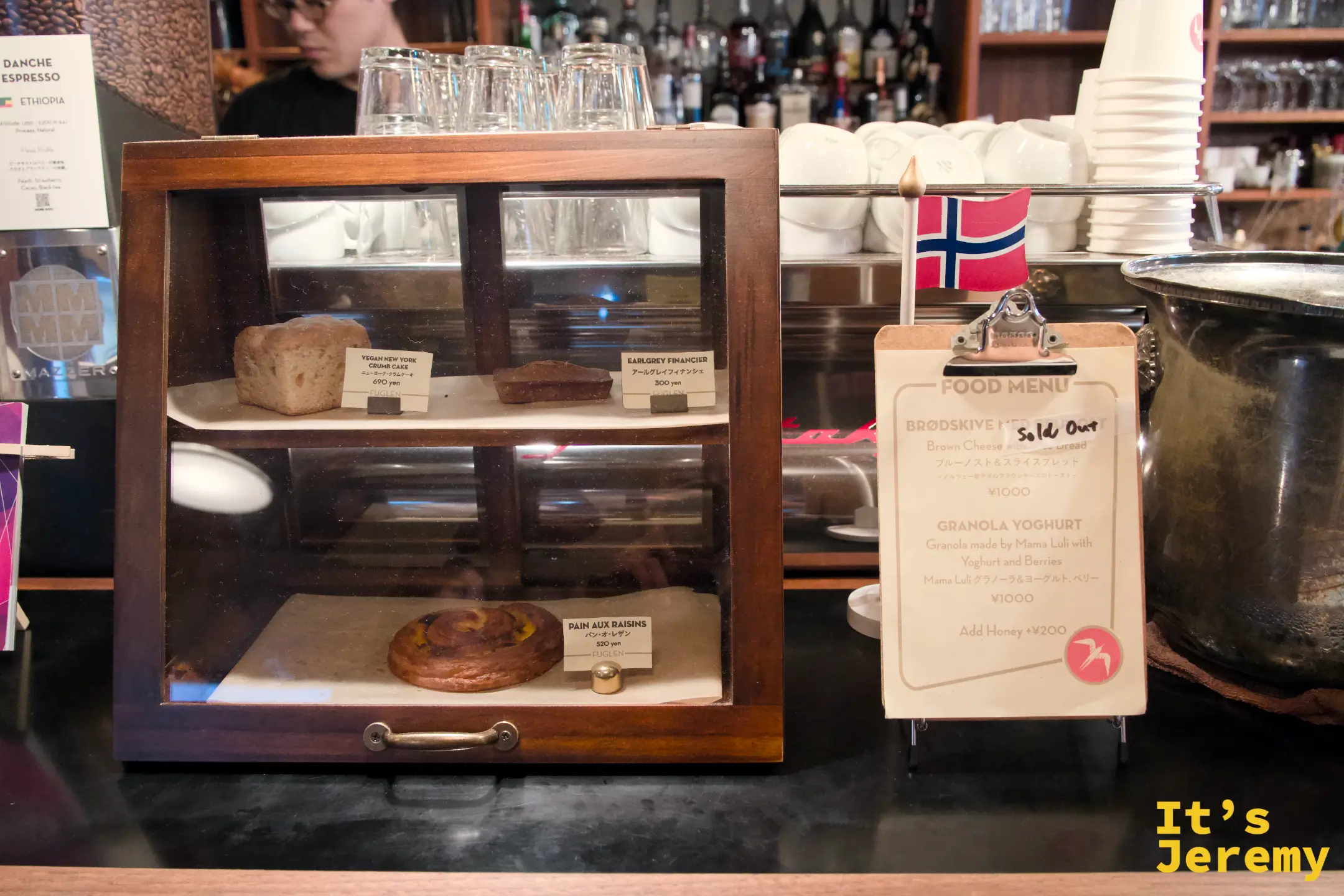 點心展示櫃:Pain aux Raisins、Earl Grey Financier、Vegan NY Crumb Cake,旁邊掛著挪威國旗和 Food Menu 看板