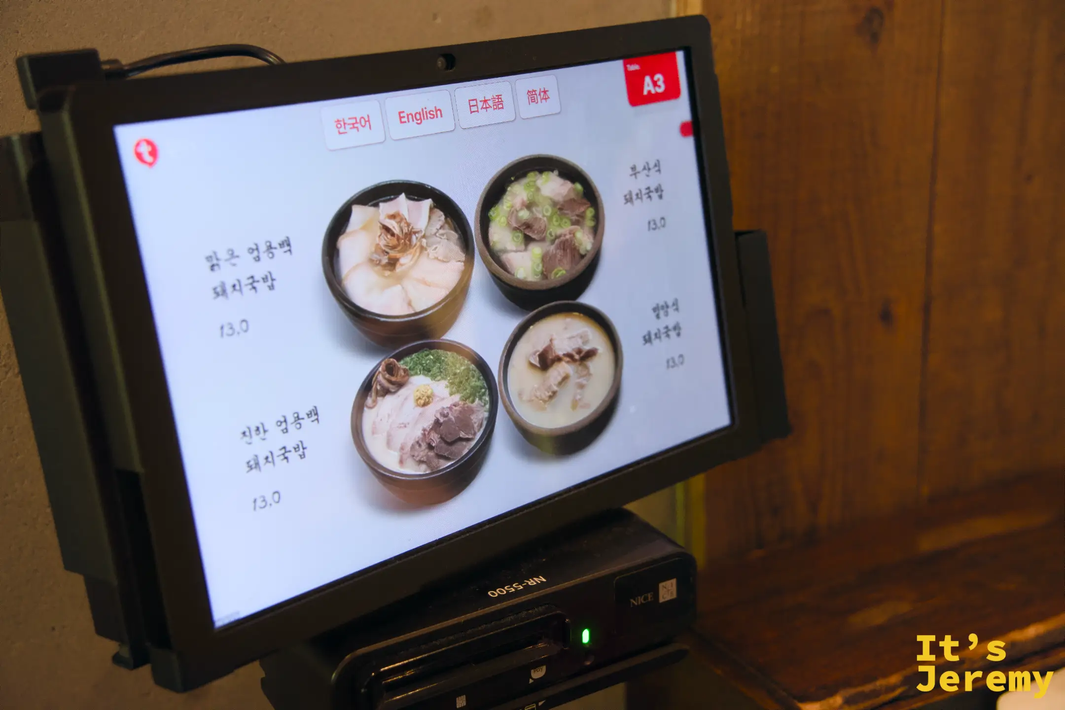 座位桌上的平板點餐機，顯示四款豬肉湯飯選項與照片，介面提供韓英日中四種語言