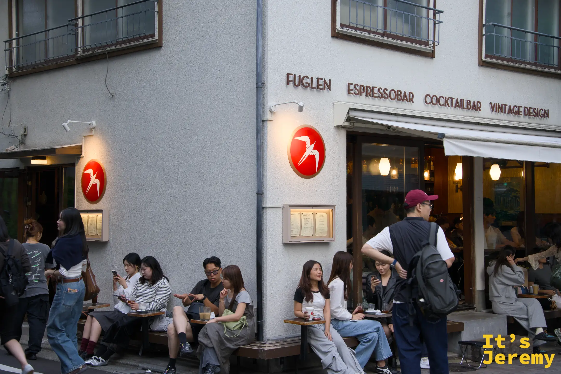 傍晚時分 Fuglen Tokyo 外觀,門口長椅坐滿人,整棟建築點燈後有一種溫暖的北歐感