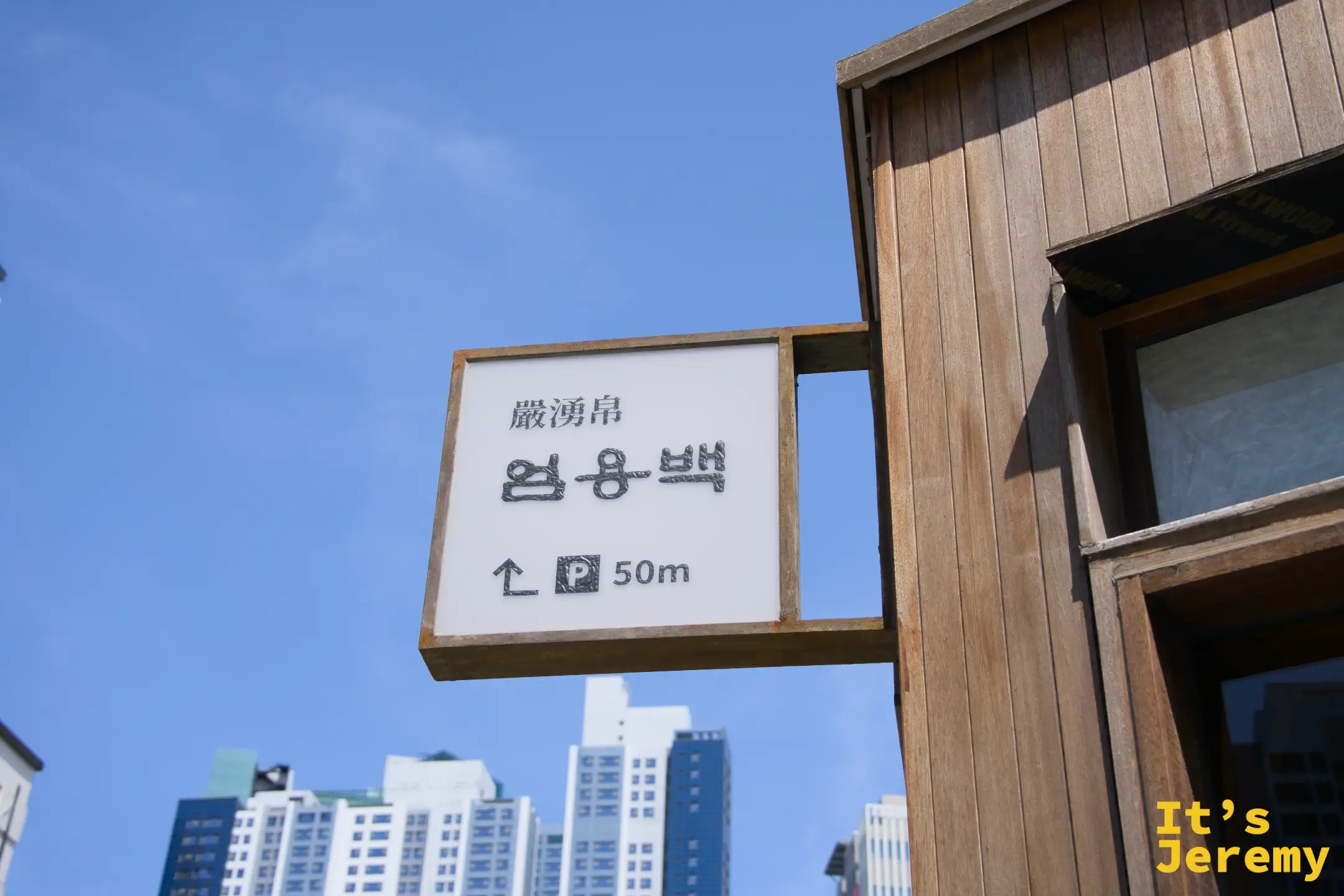 店外路標指示，漢字「嚴湧帛」清晰可見，藍天下簡潔俐落的木框招牌