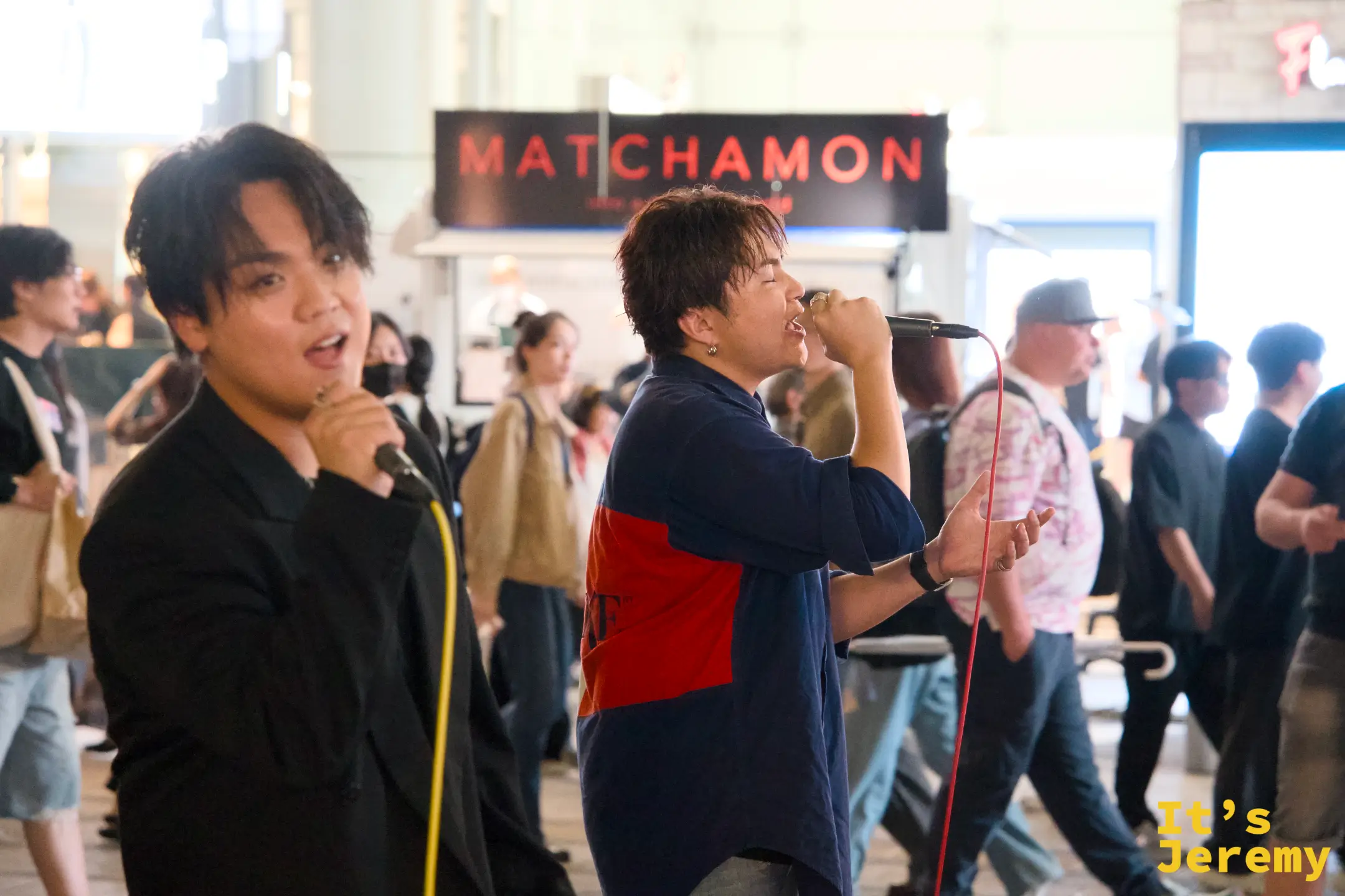 歌舞伎町セントラルロード旁的街頭表演,「MATCHAMON」橫幅高掛,兩位年輕男性拿麥克風熱情演唱,路人在旁圍觀