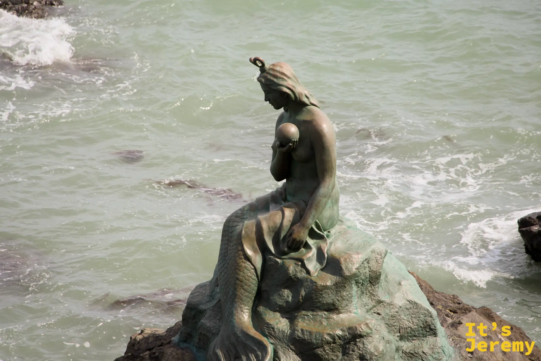 冬柏島人魚銅像，坐在礁石上望向大海，墨綠色氧化銅質地與海浪相映