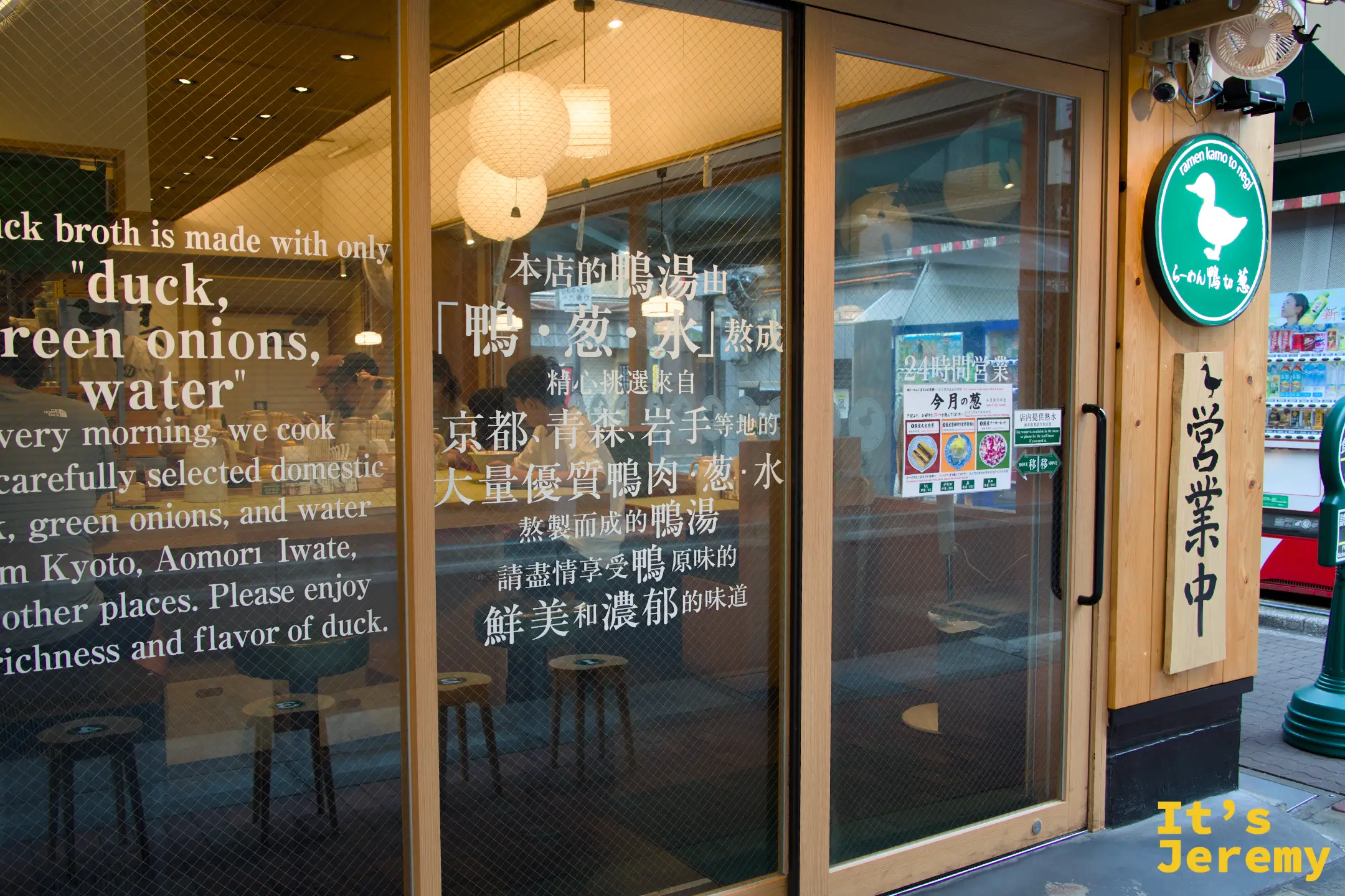 店門玻璃特寫，貼著「本店的鴨湯由鴨・蔥・水熬成」中日英三語說明