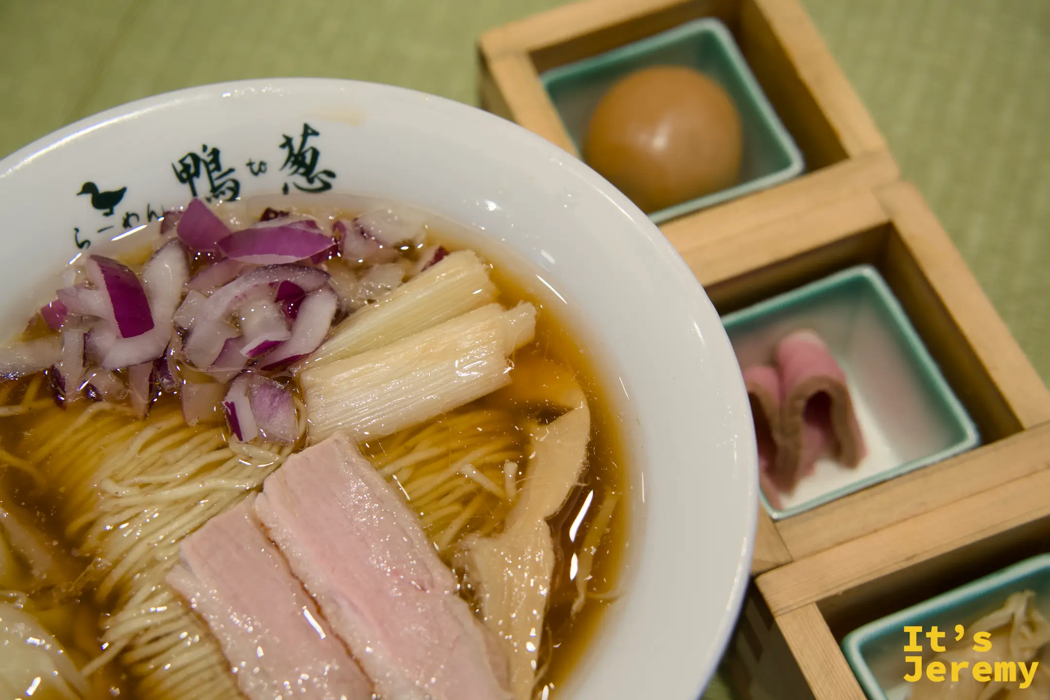 鴨らーめん特上近景，清醬油湯底盛著細麵，鴨肉片與紅洋蔥鋪在上方，旁邊木盒裝著溏心蛋和鴨コンフィ