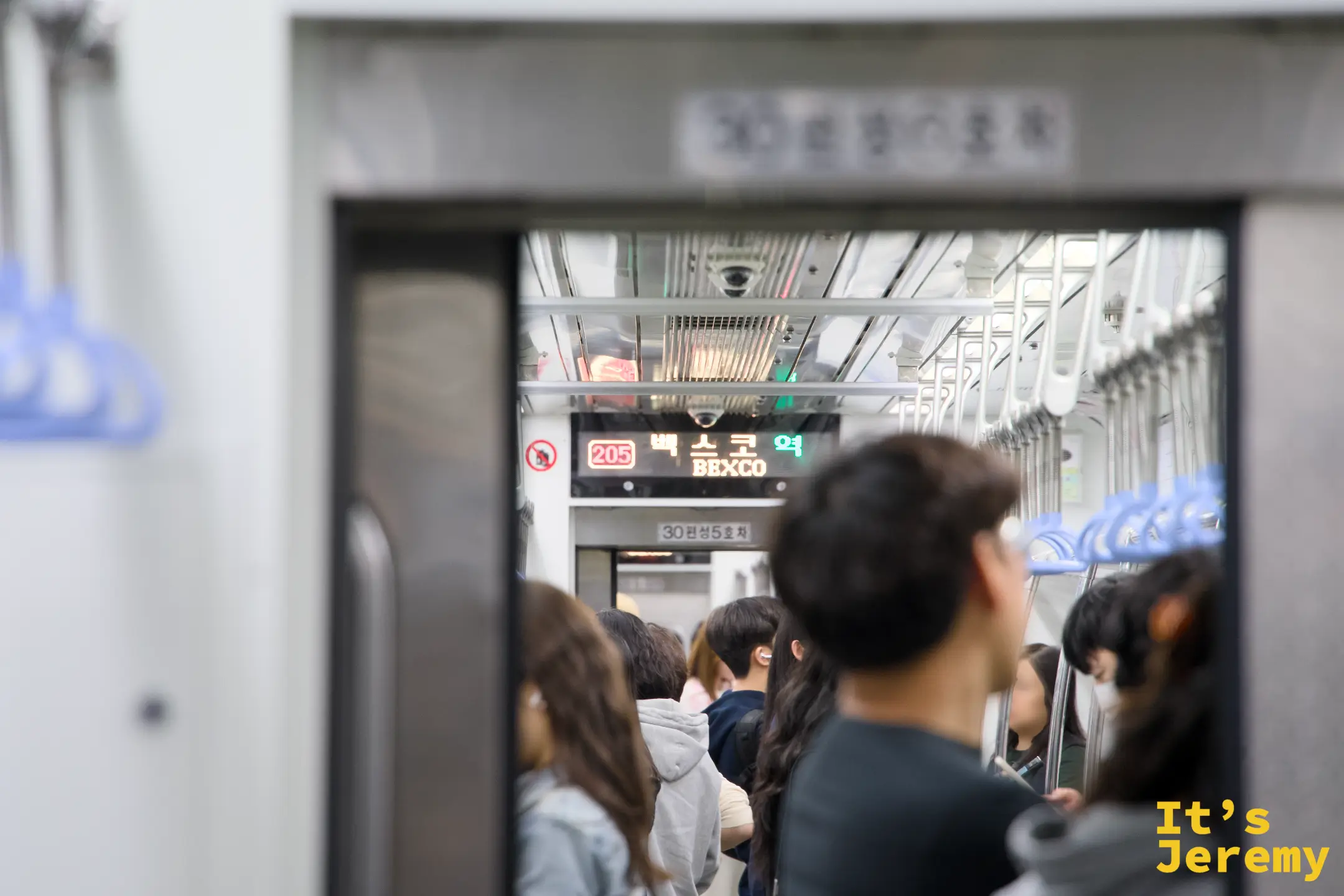 地鐵 2 號線車廂內,頭頂顯示板亮著「벡스코 역 BEXCO」——車廂裡站滿週末出遊的人潮,再過幾站就是廣安里