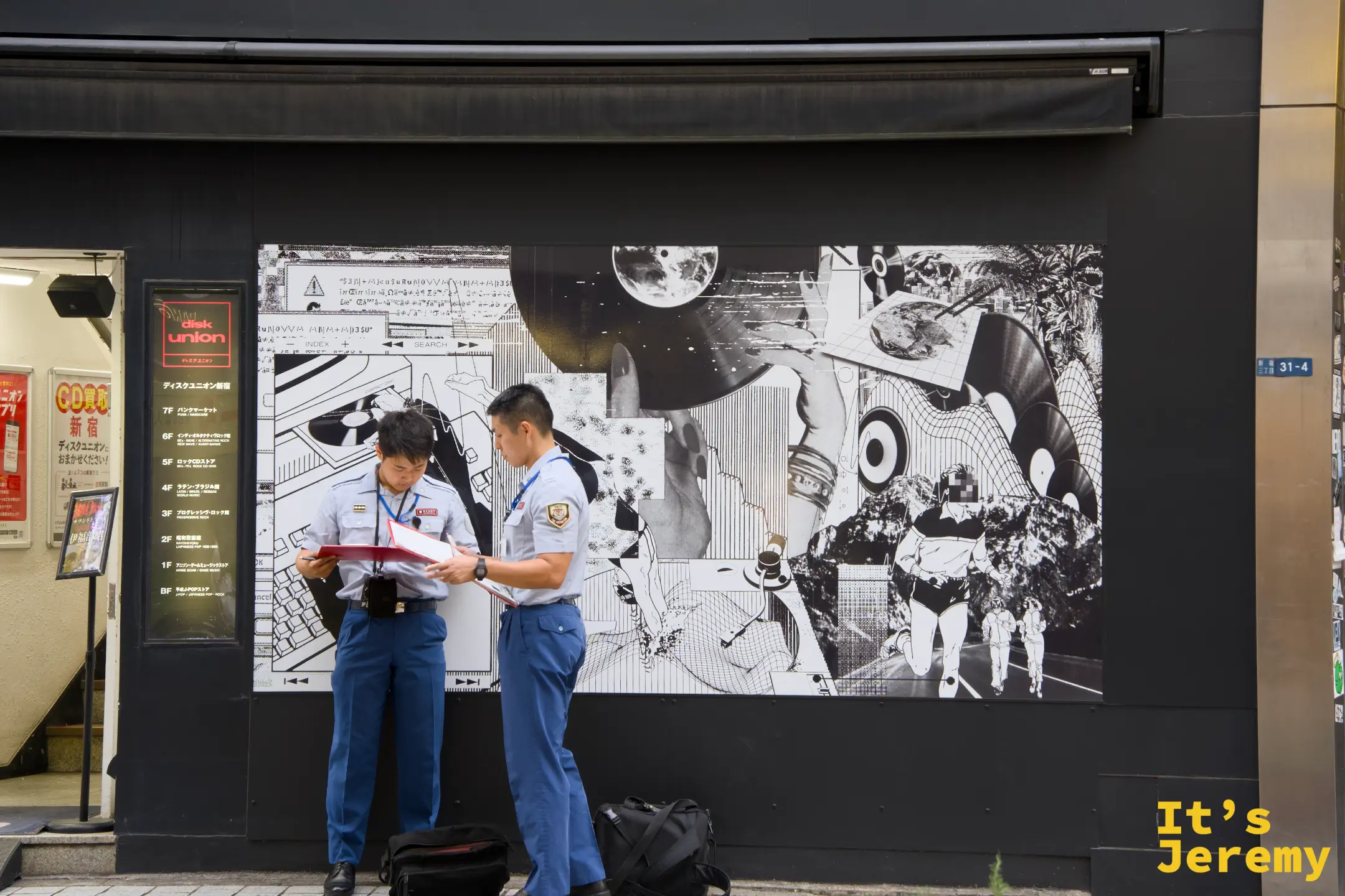 DiskUnion 新宿店外,兩名警察低頭核對文件,身後是店家外牆的大型黑白拼貼壁畫