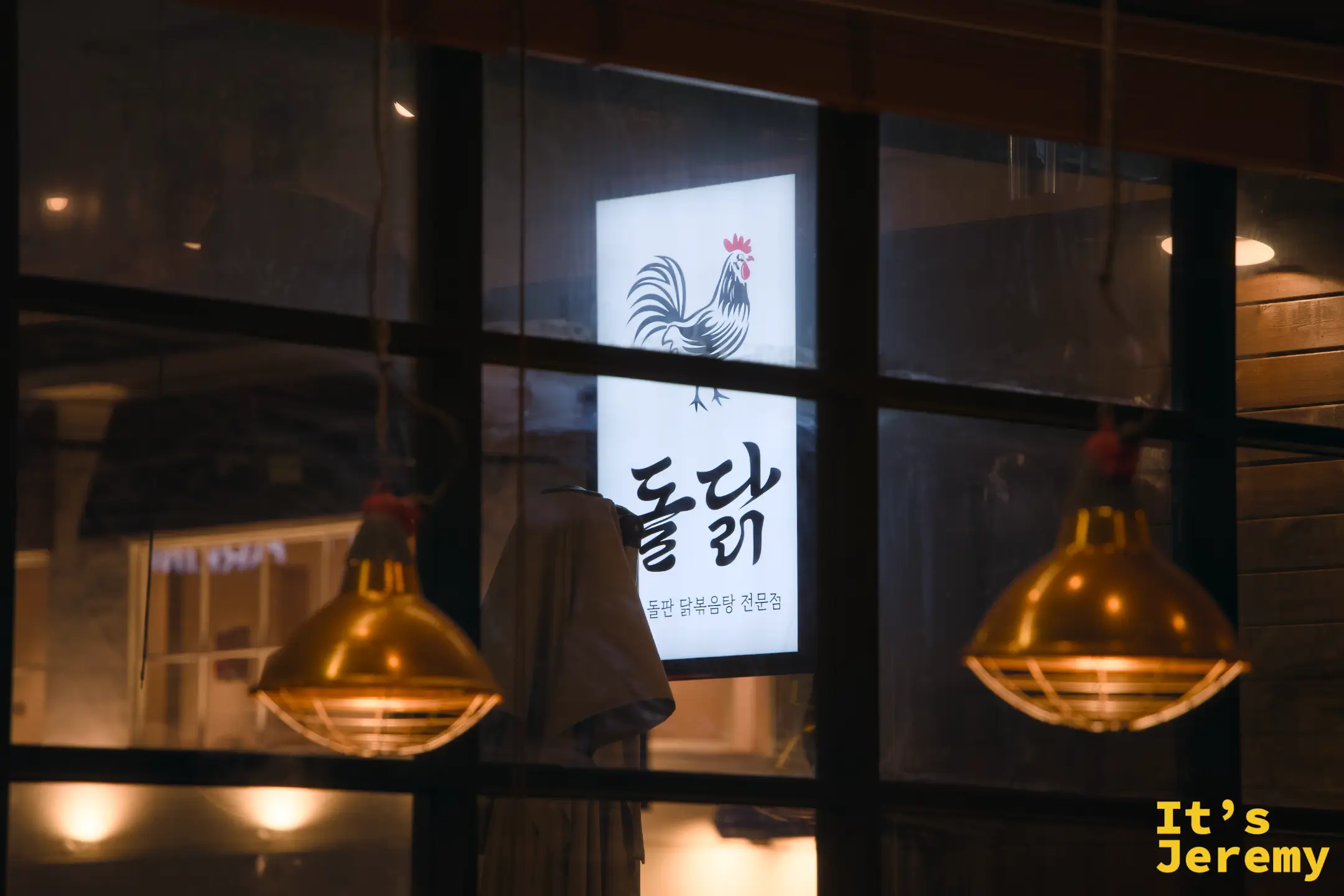 入夜後的돌닭門面，銅燈打出暖光，玻璃窗映出公雞招牌，氛圍感滿分