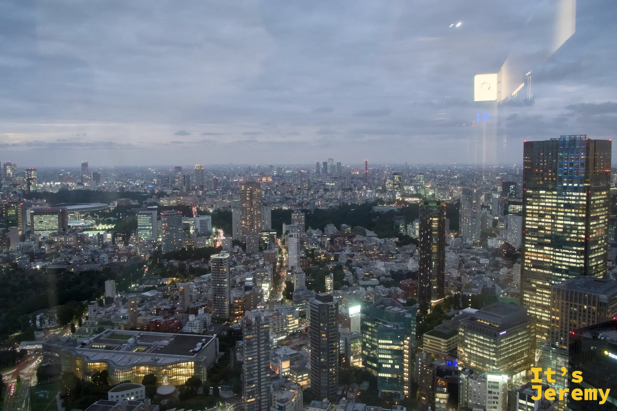 透過展廳玻璃窗望向東京黃昏全景，遠處可見東京鐵塔細長的輪廓