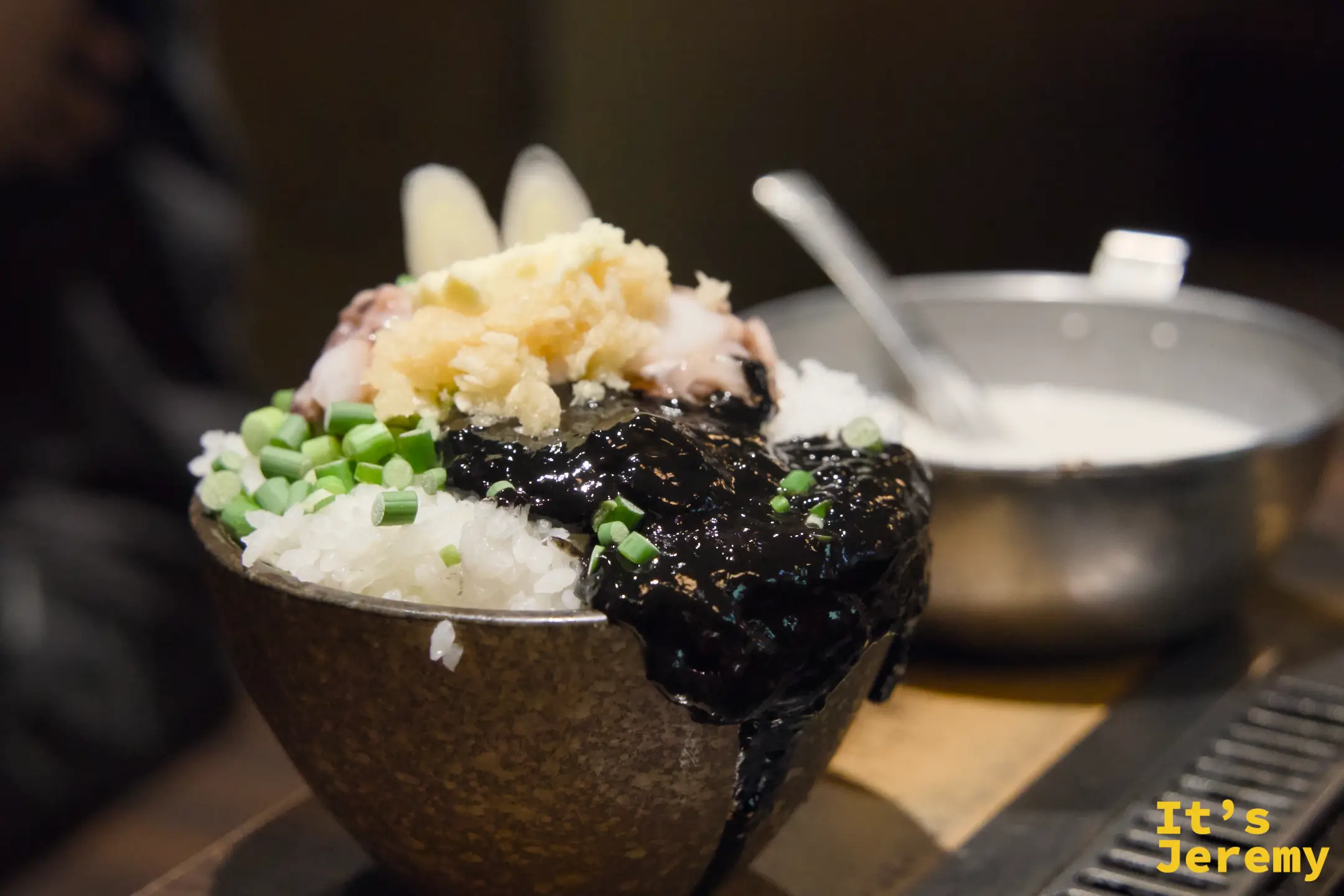 いか墨もんじゃ的食材在石碗裡，墨黑的醬汁裡有烏賊足和青蔥