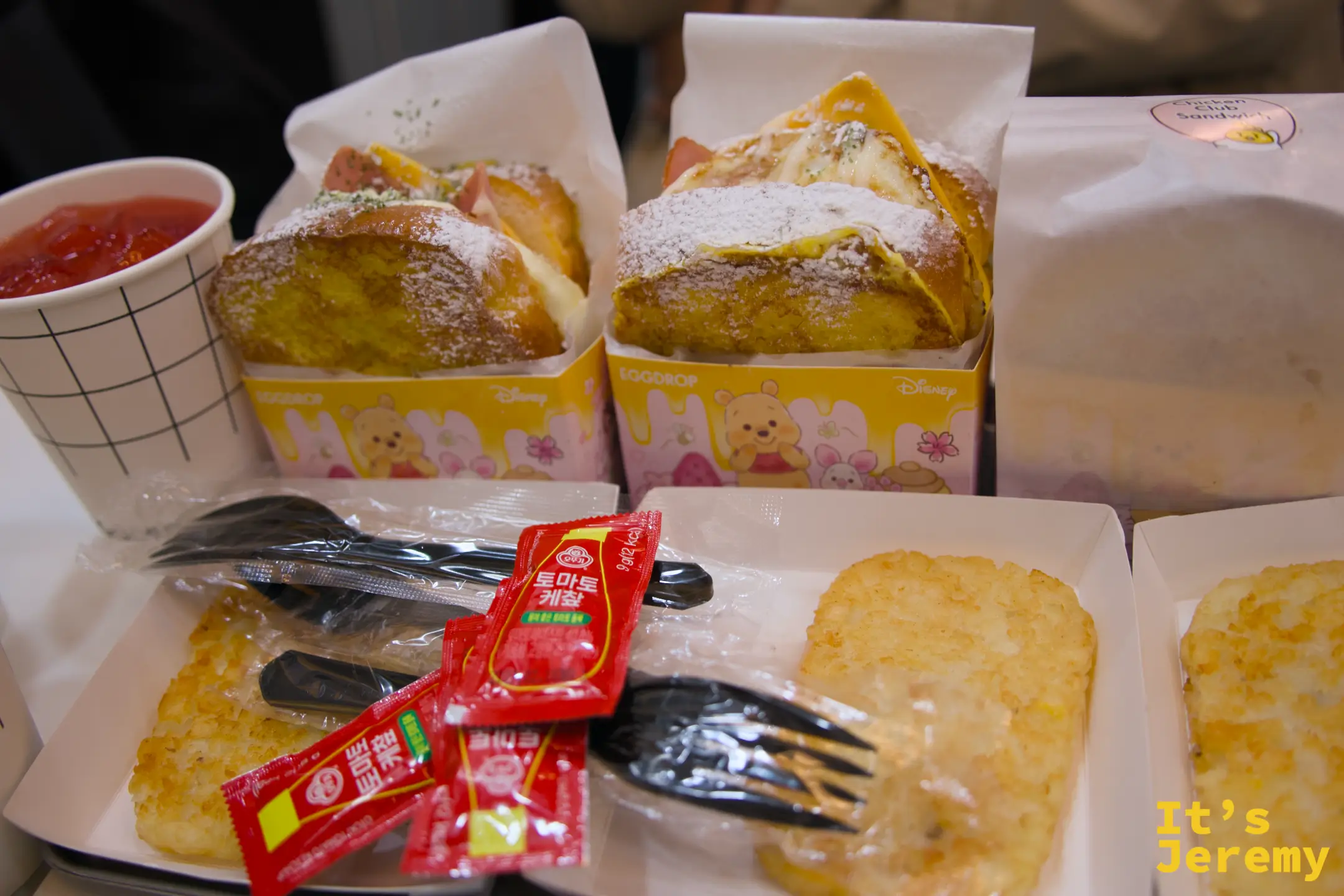桌上的全餐：兩份法式吐司、薯餅、西瓜汁，Disney 聯名紙盒搭配白底格紋杯一起上桌