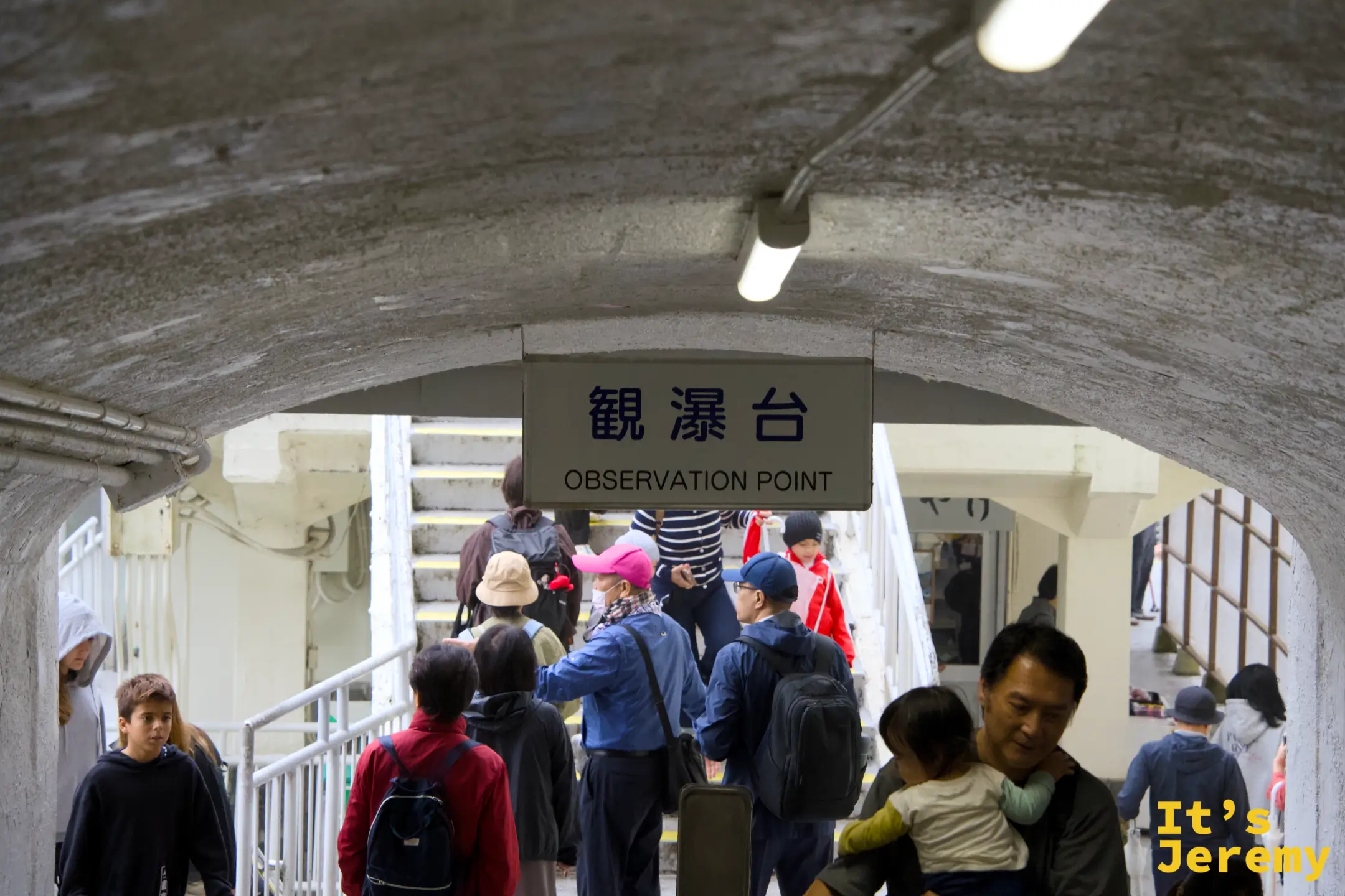 地下觀瀑台通道入口，拱形走廊上掛著「觀瀑台 Observation Point」指示牌，人潮正要走向瀑布
