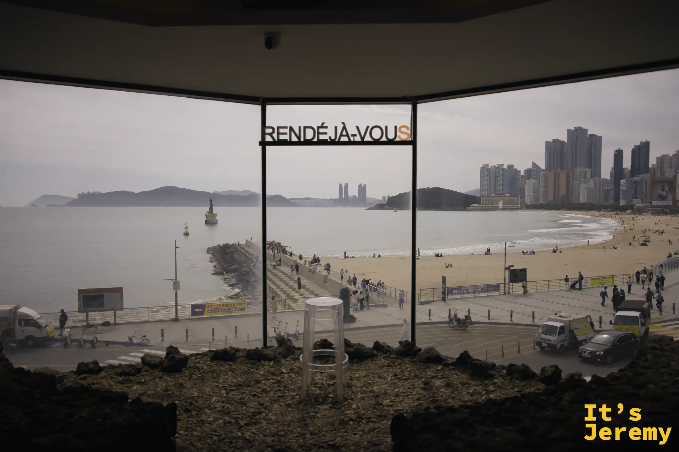 RENDÉJÀ-VOUS logo 懸掛在落地窗鐵框上，窗外是海雲台防波堤全景