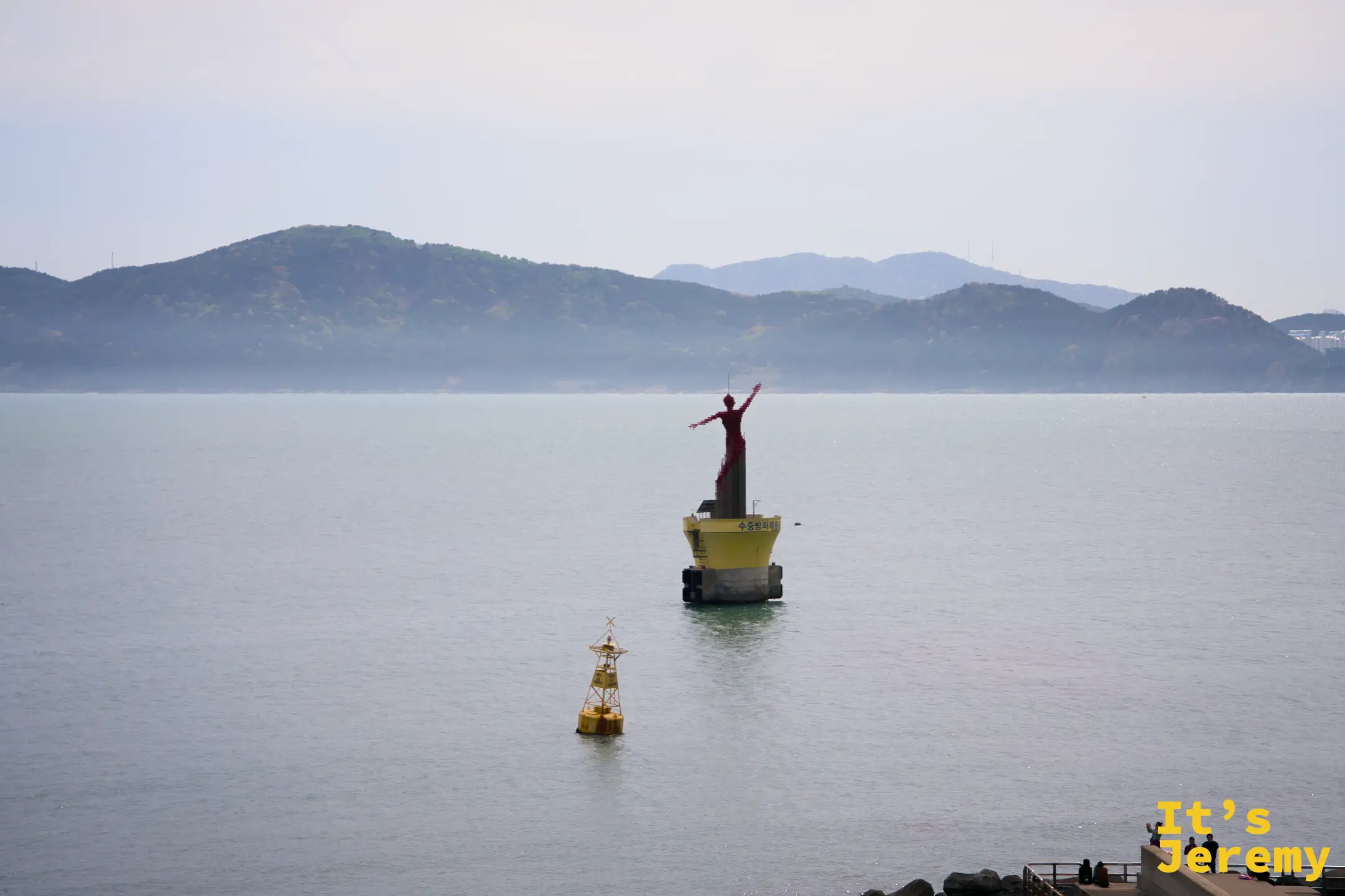 從咖啡廳窗邊遠眺，防波堤末端的紅色女神守護像佇立海中