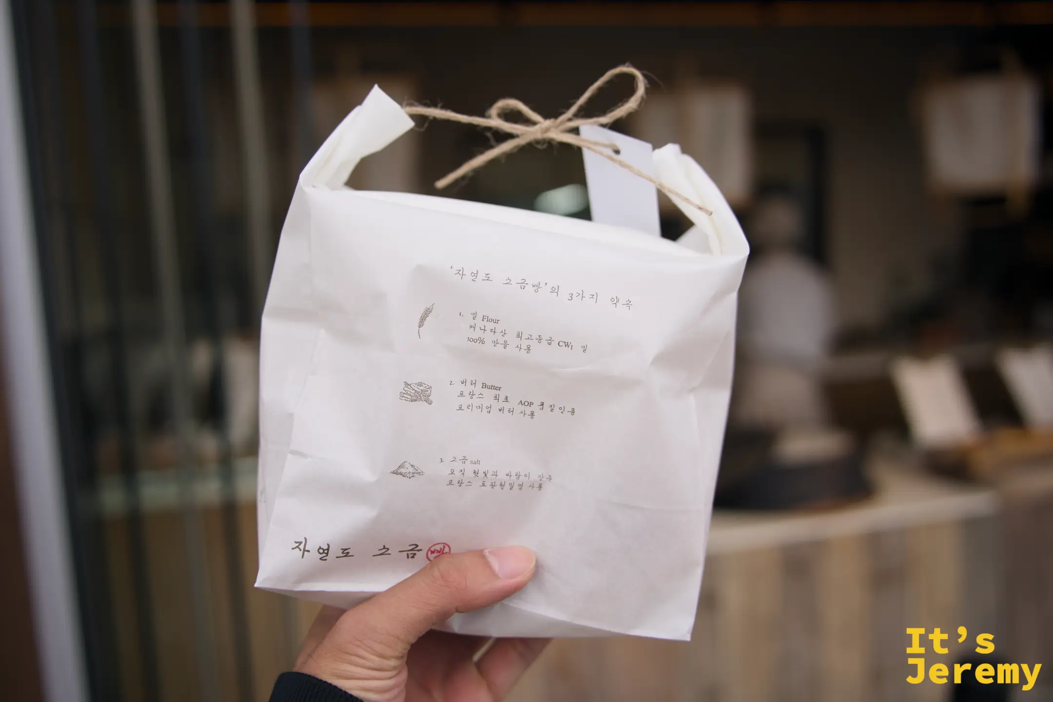 手持印著三大承諾的자연도 소금빵白色禮袋，麻繩蝴蝶結扣頂
